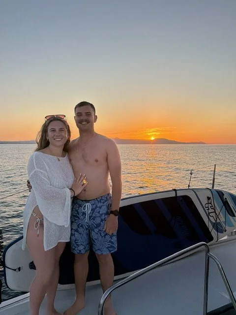 Kyra and Luke smiling on a sunset boat ride during their Greece honeymoon.