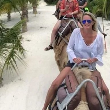 Group of people riding camels through a sandy desert with palm trees.