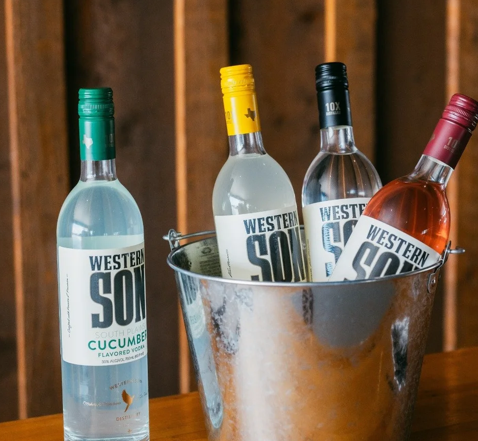 Four bottles of Western Son flavored vodka, including cucumber and other flavors, in a metal bucket on a wooden surface.