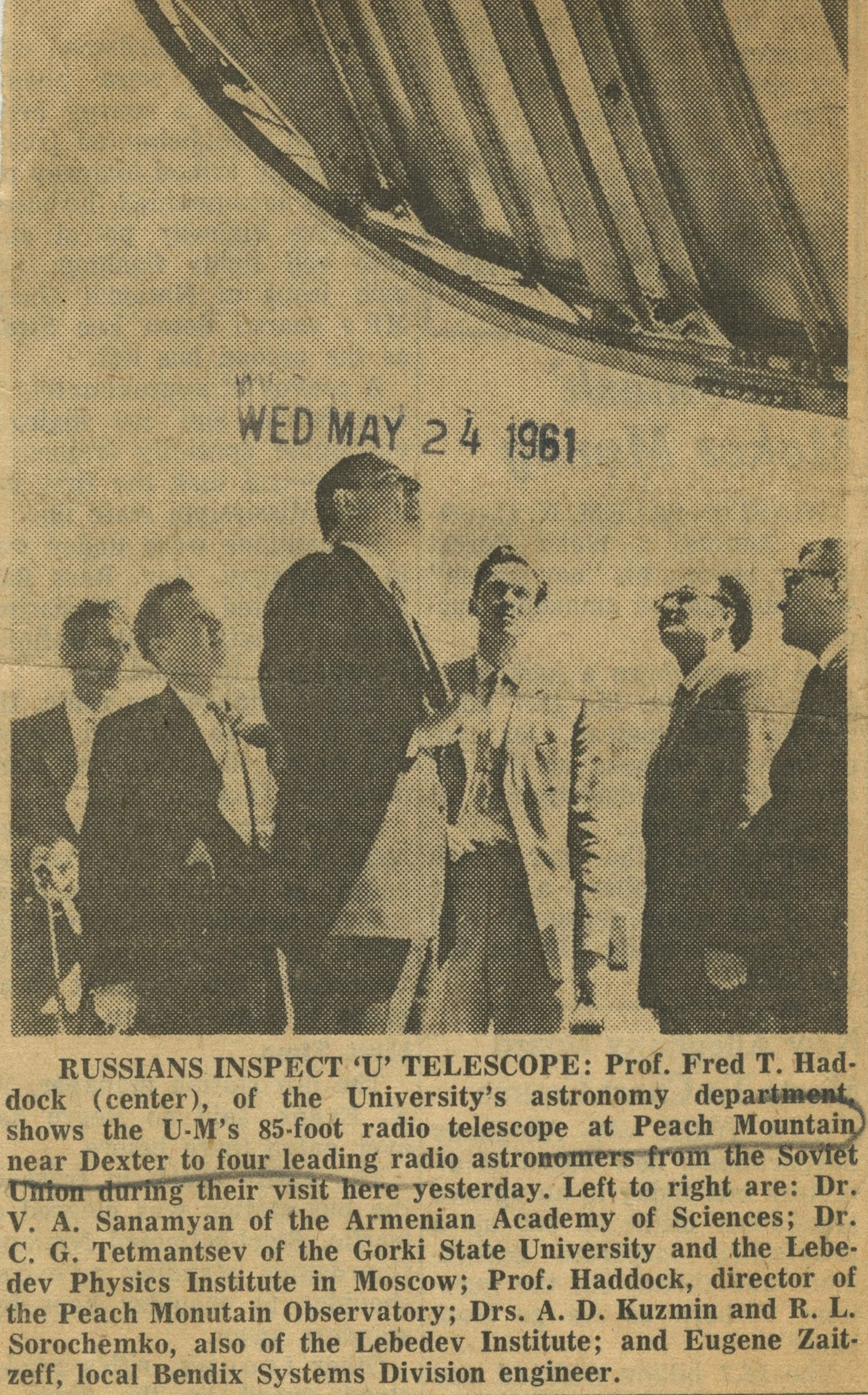 Black and white photo of a group of men, including Prof. Fred T. Haddock, inspecting a 85-foot radio telescope at Peach Mountain near Dexter, on Wednesday, May 24, 1961, with a large overhanging structure above them.