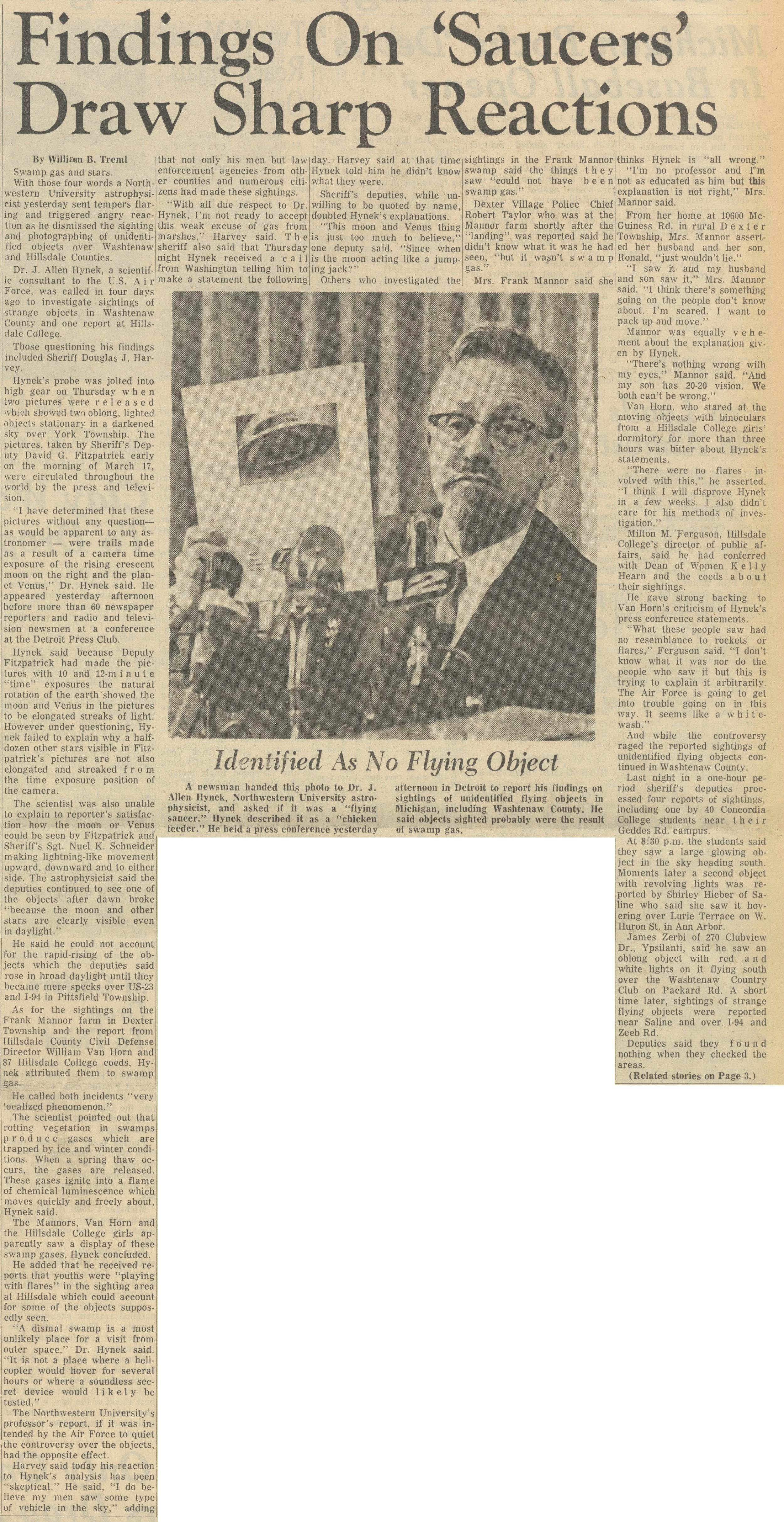 Photograph of unidentified man at a press conference, with a microphone in front of him, in a room with tall windows and other people present.