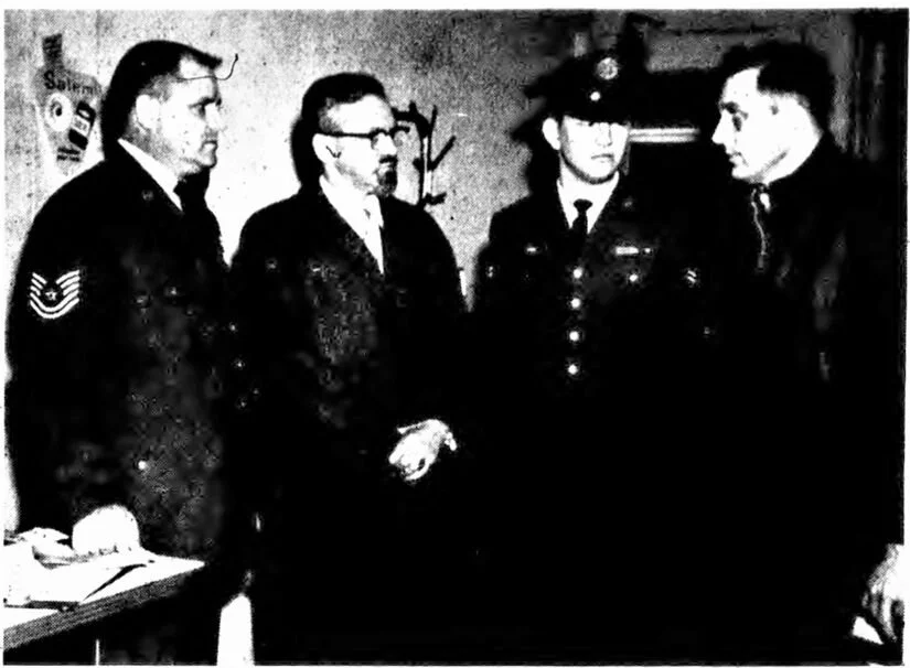 Four individuals in military uniforms engaging in conversation indoors.