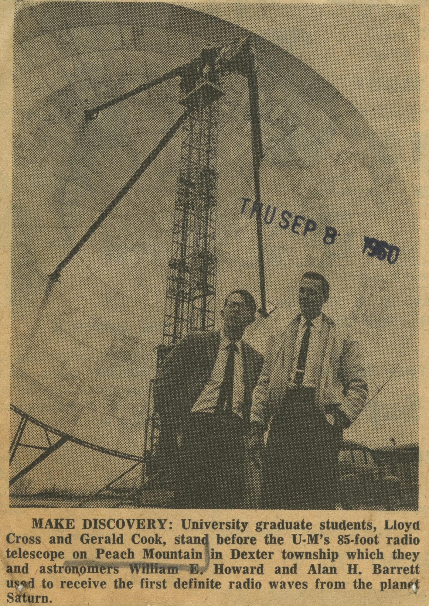 Two university students, Lloyd Cross and Gerald Cook, standing in front of a tall U-M 85-foot radio telescope on Peach Mountain in Dexter township, with a sign that reads "THU SEP 8 1950." They are dressed in suits and ties, smiling at the camera.