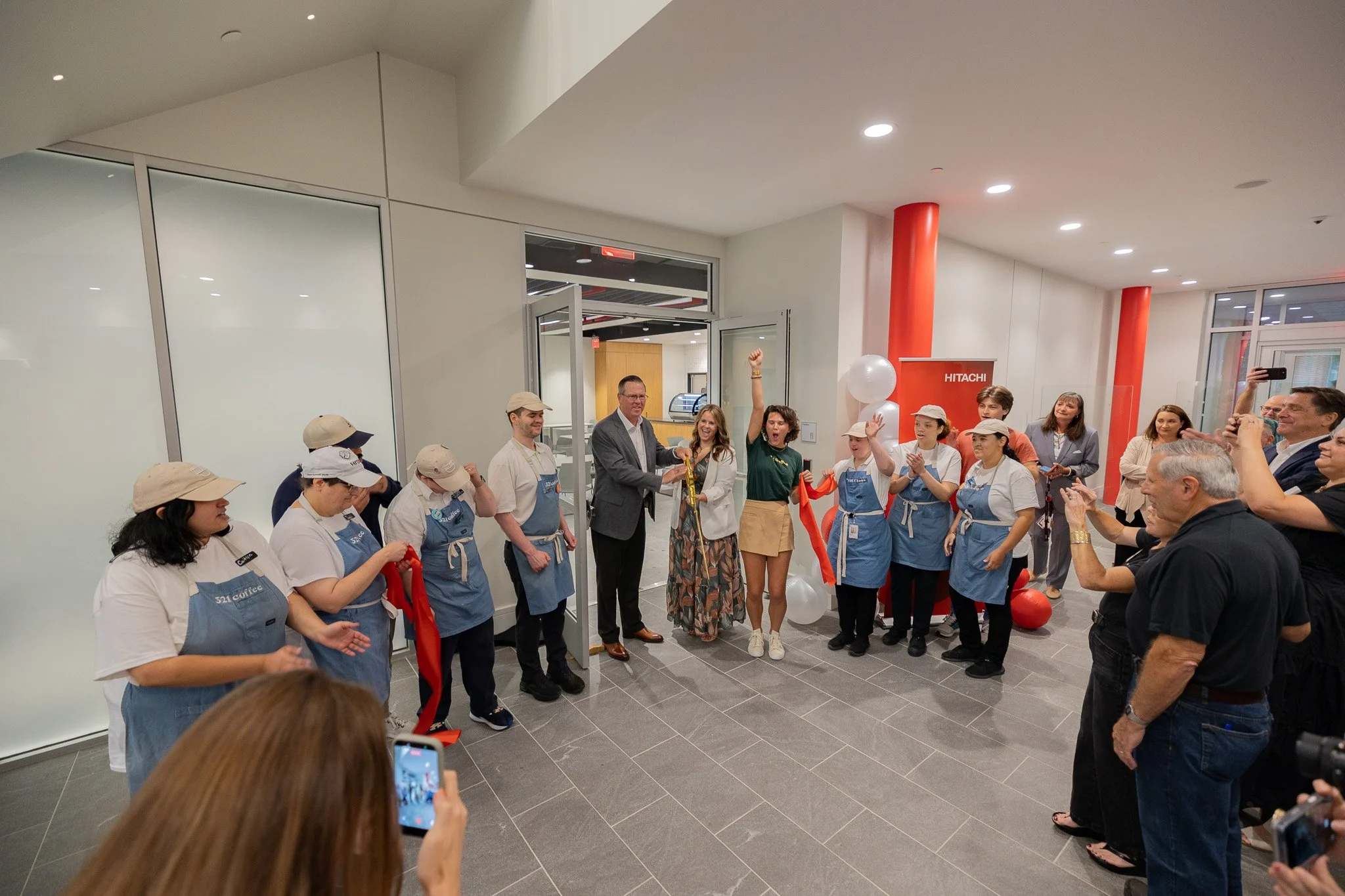 Members of the 321 Coffee and Hitachi Energy teams celebrate with smiles and their hands in the air moments after cutting the ribbon to the new cafe.