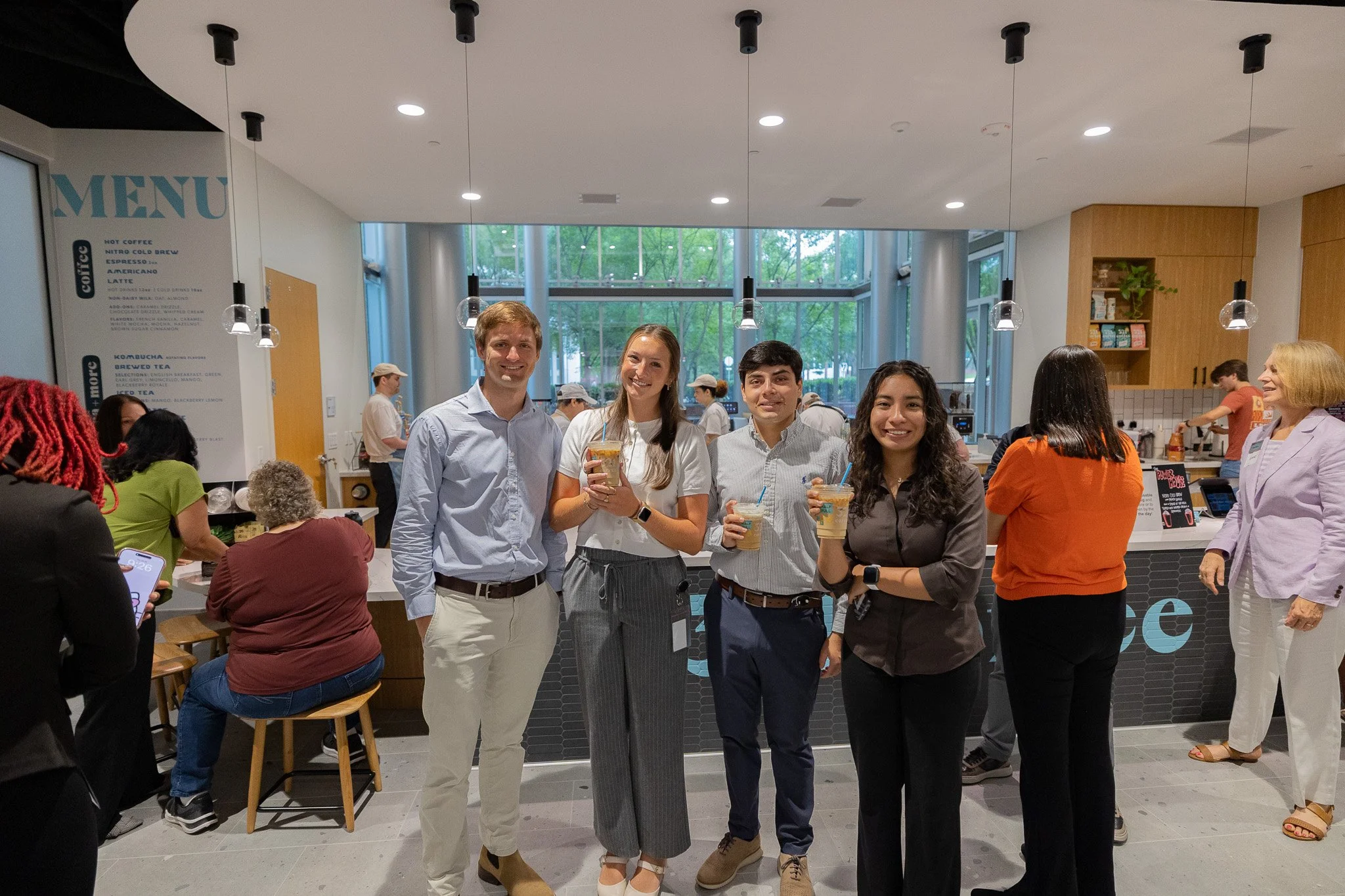 Four Hitachi team members smile for a photo while standing in front of the cafe and enjoying iced lattes at the office.