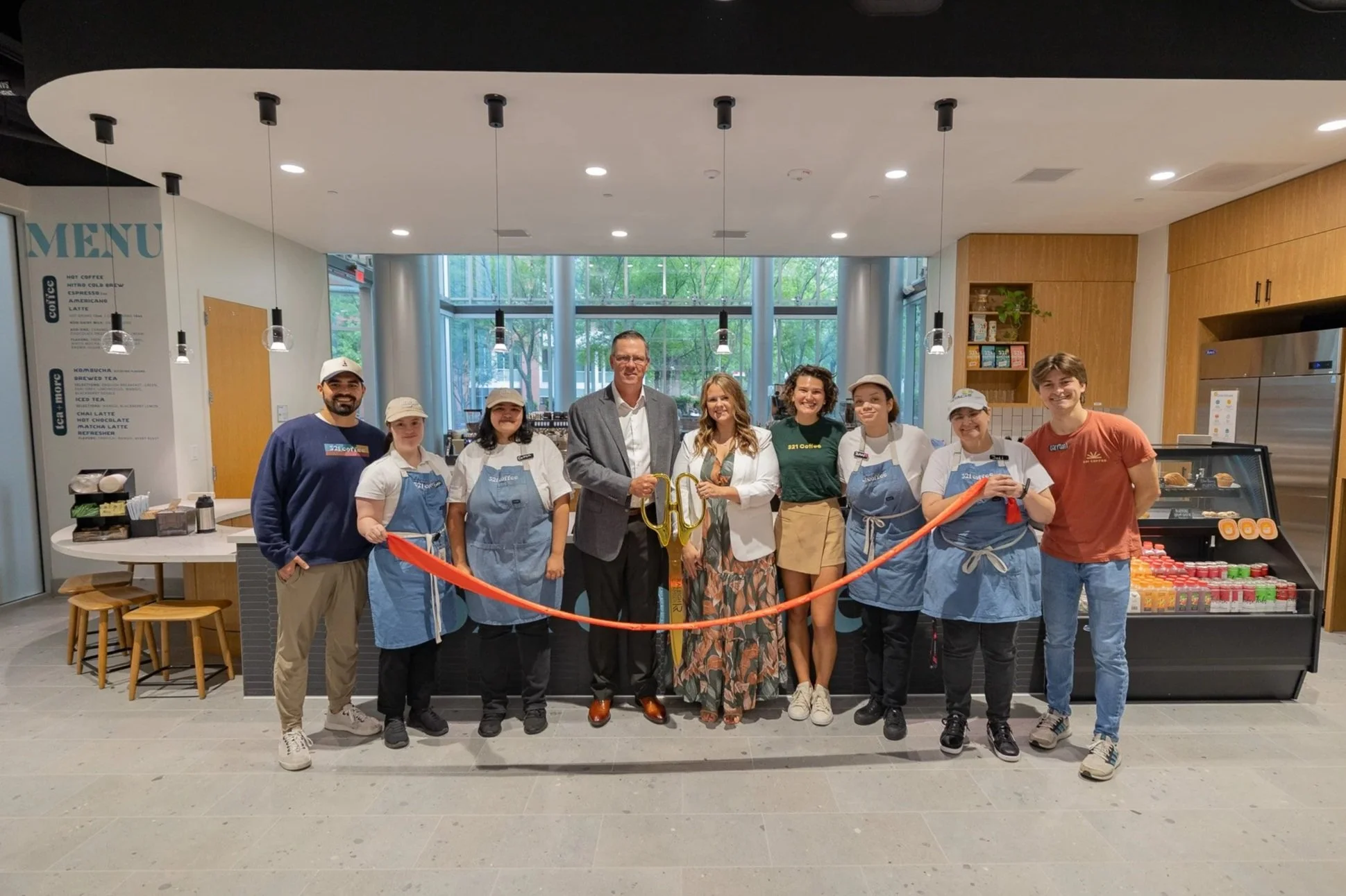Members of the Hitachi Energy and 321 Coffee teams gather in front of the new cafe and hold a red ribbon in preparation for the ribbon cutting celebration.
