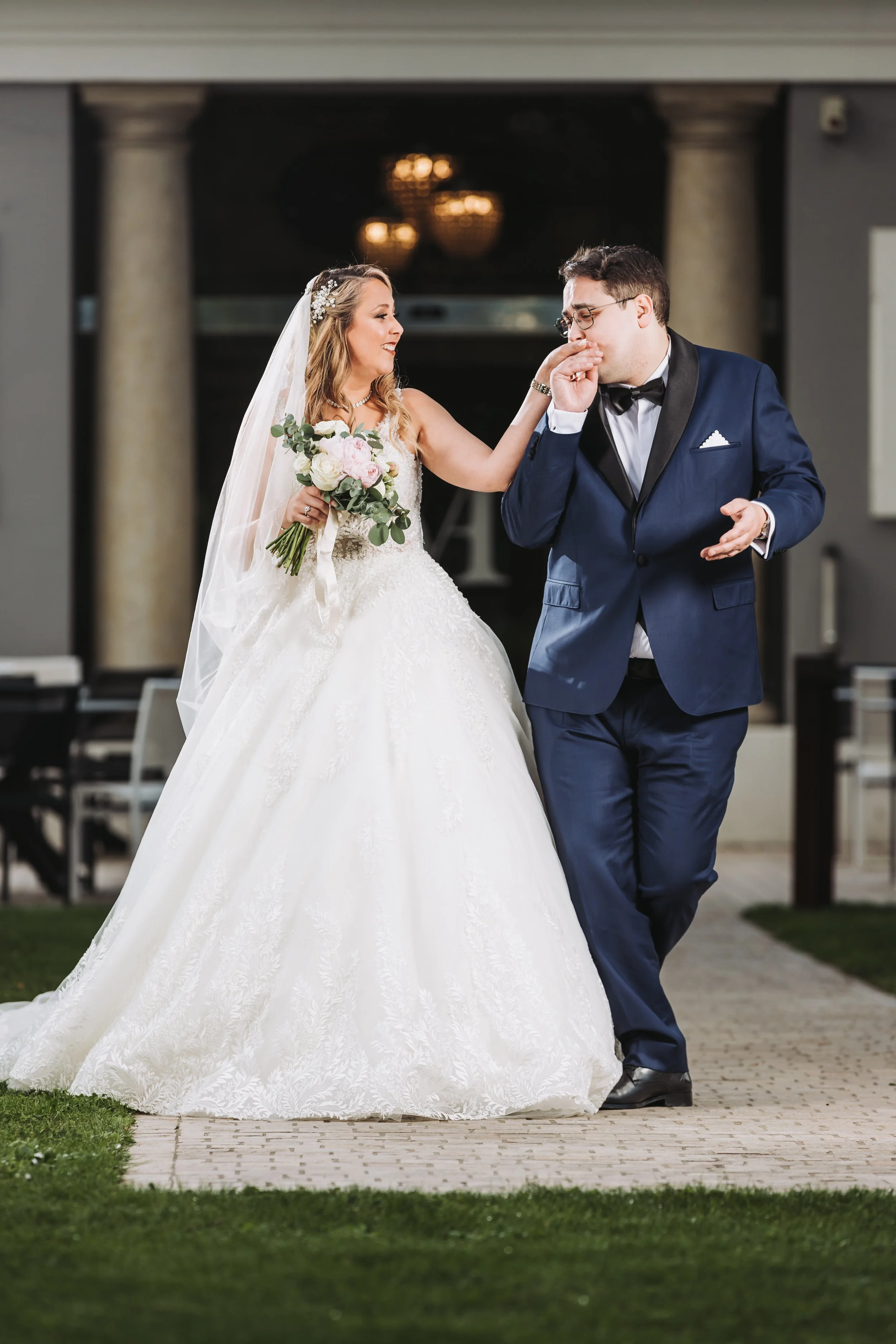 Le marié embrasse la main de la mariée devant la colonnade de la Maison d'Anthouard