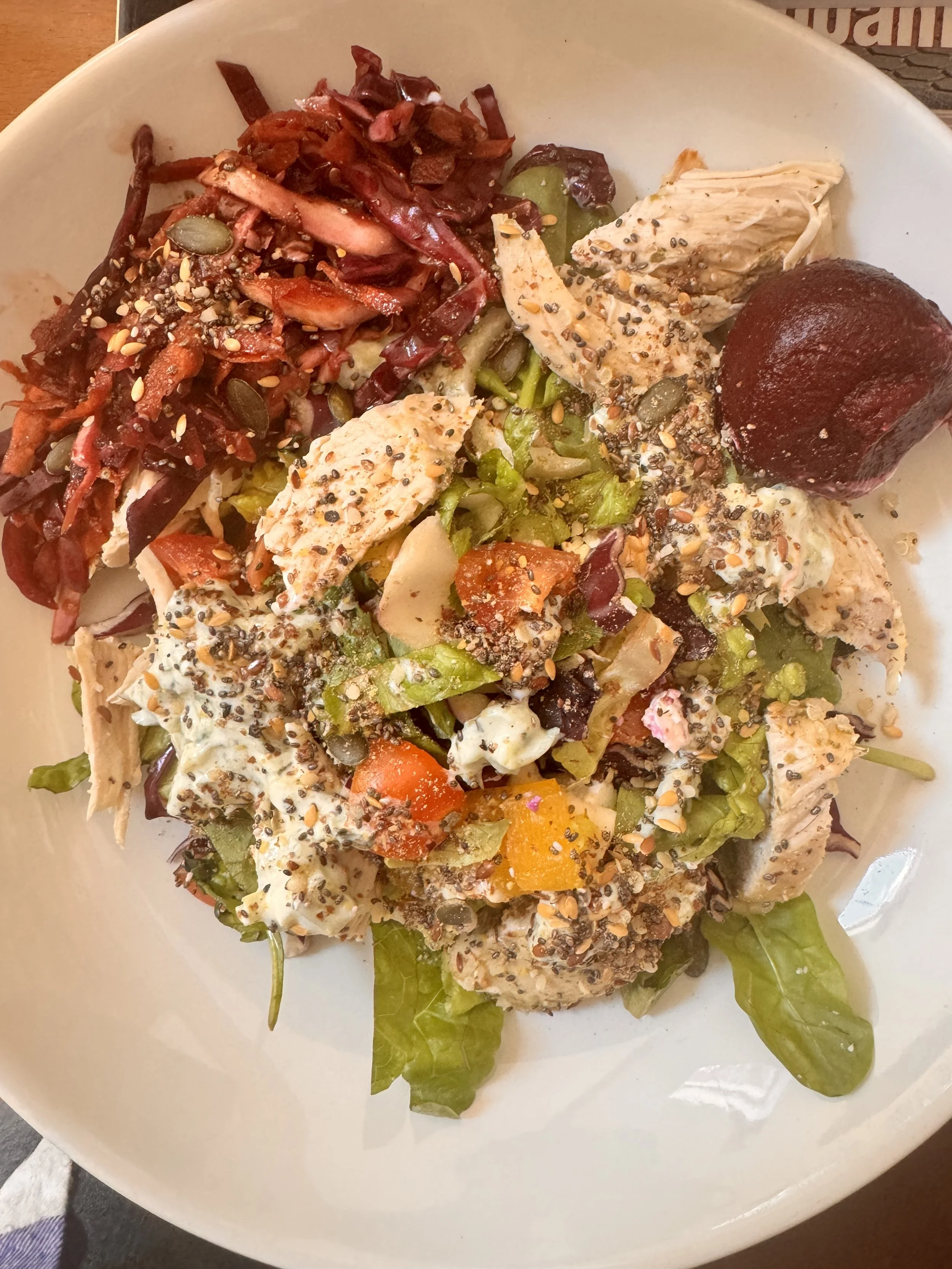 Salad with lettuce, cherry tomatoes, shredded chicken, beets, shredded carrots, and seeds, topped with dressing and black pepper.