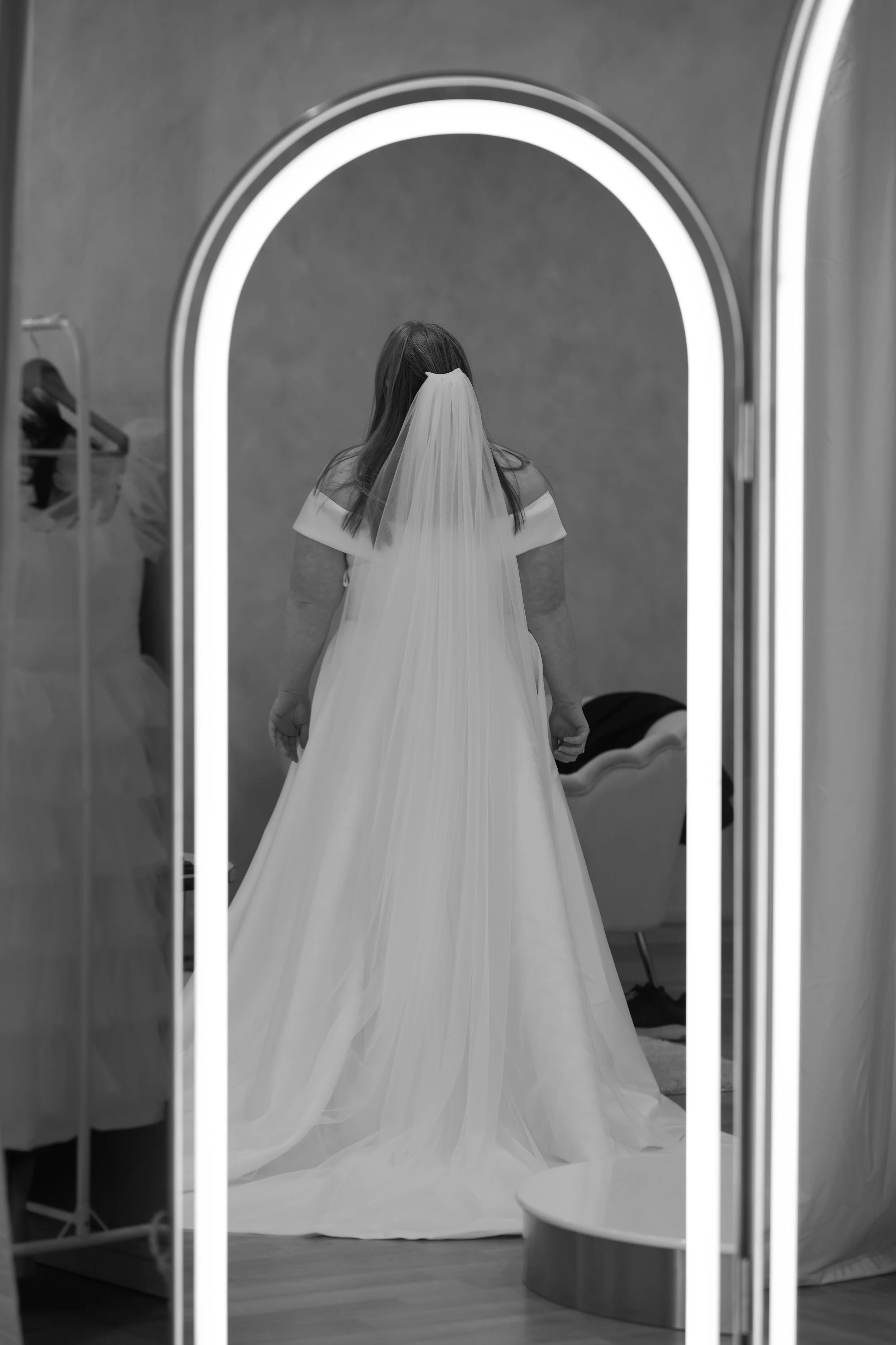 A woman wearing a wedding dress with a veil, standing in front of a mirror.