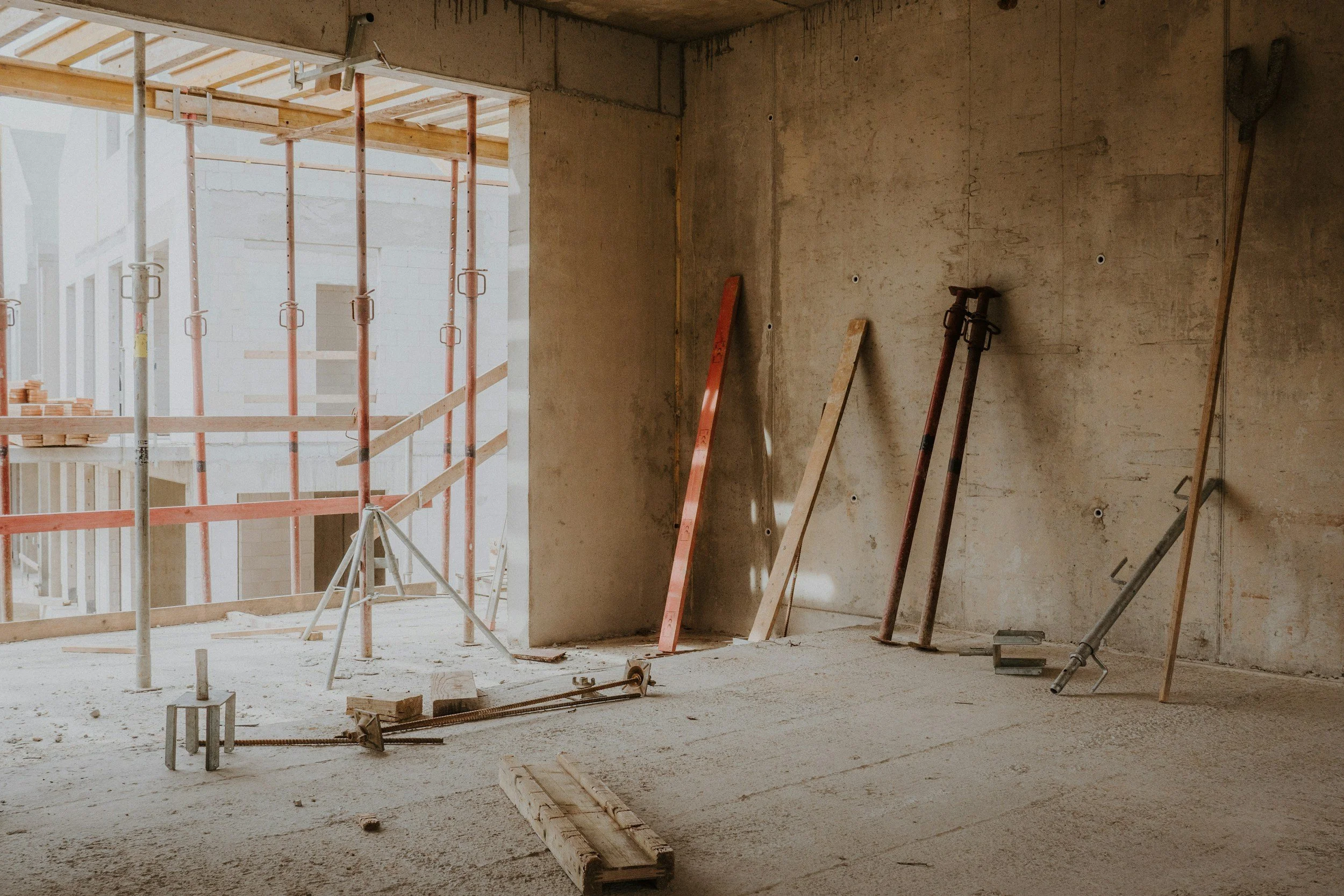 Interior of a building under construction, with scaffolding and construction tools leaning against the wall.