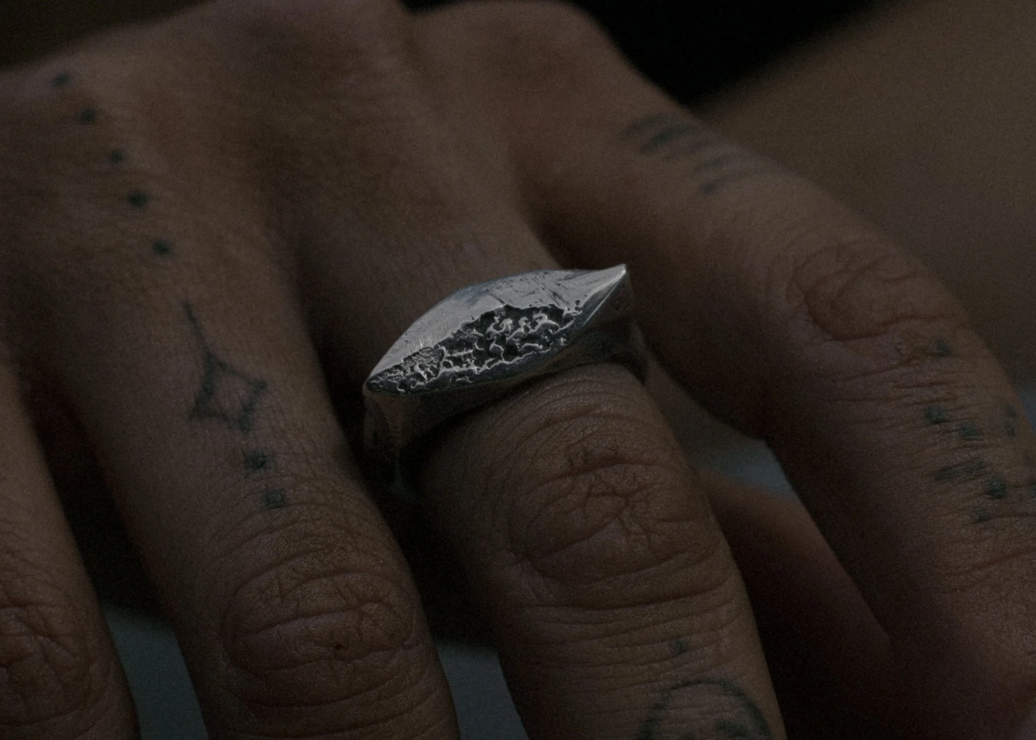 Close-up of a hand wearing a dark metal ring with a textured, leaf-shaped face