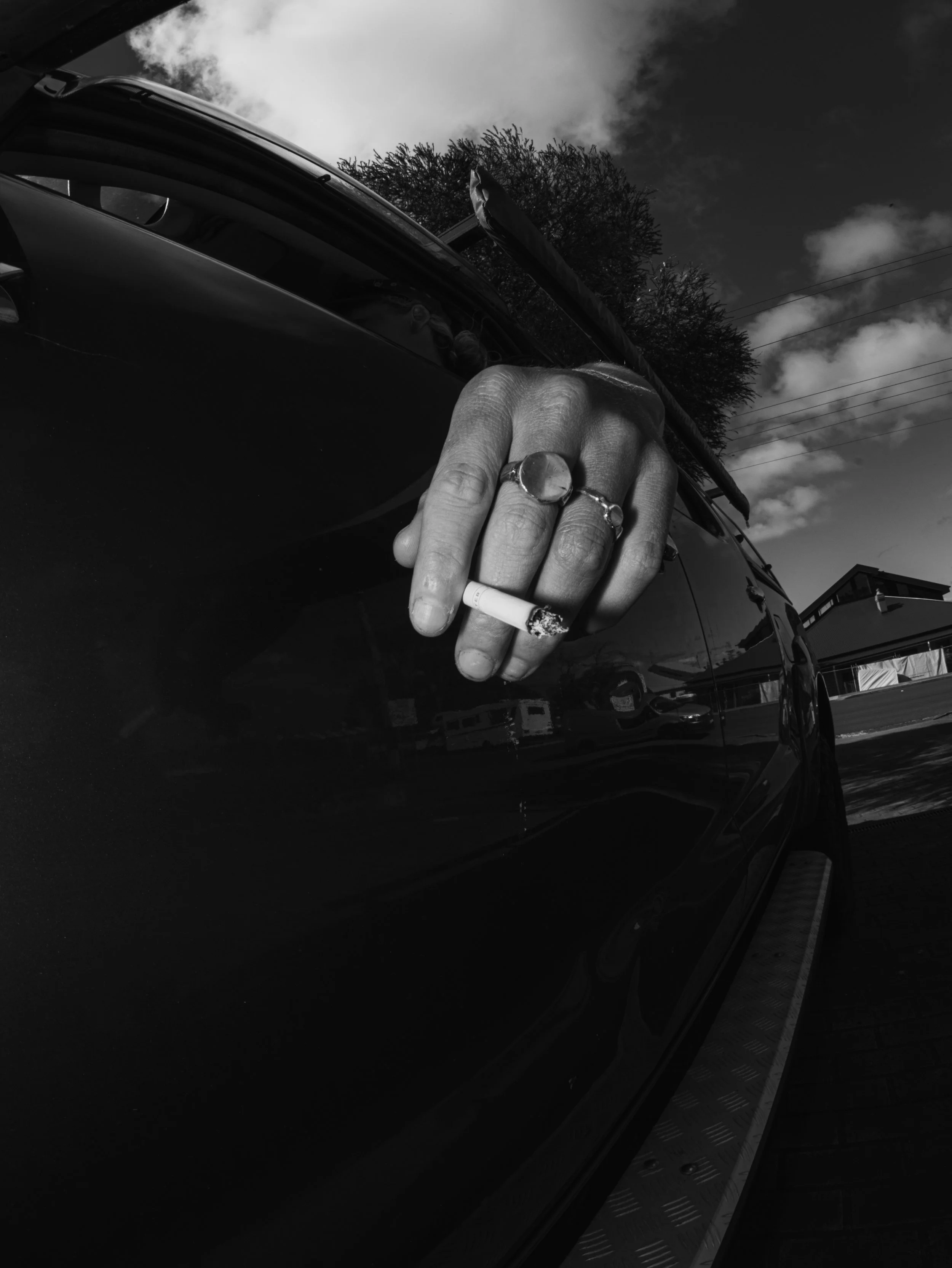 Black-and-white close-up of a hand holding a lit cigarette beside an open car door.