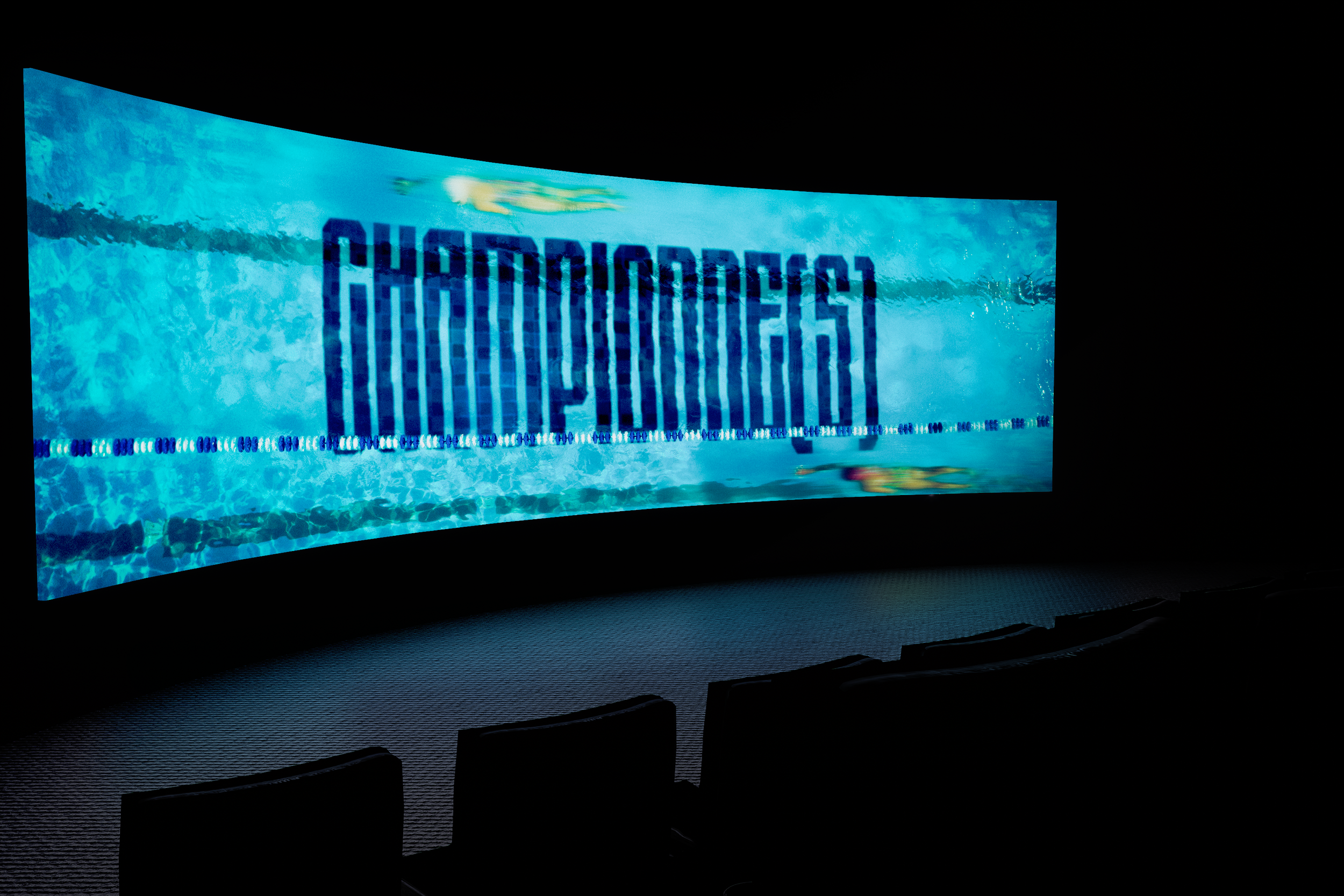 An indoor swimming pool with a digital timer reading 1:14.45, illuminated in blue and teal tones, with dark surroundings.