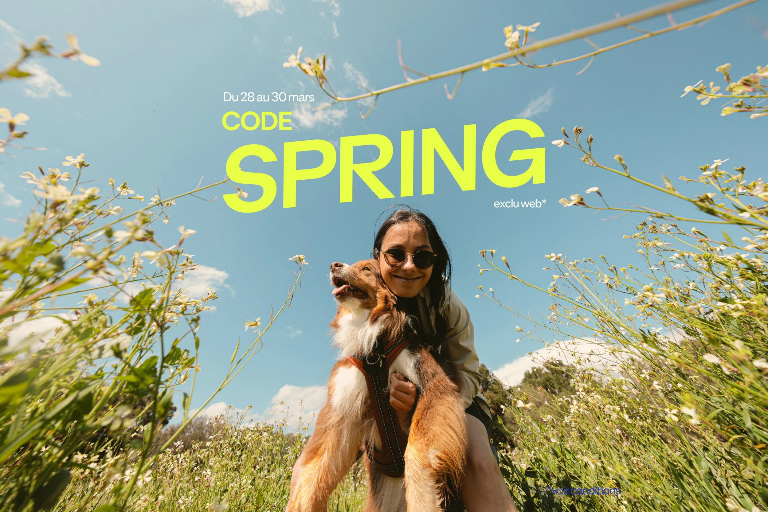 Smiling woman in glasses with an Australian Shepherd in a flower field. Code Spring, a web-exclusive event from 28 to 30 March.