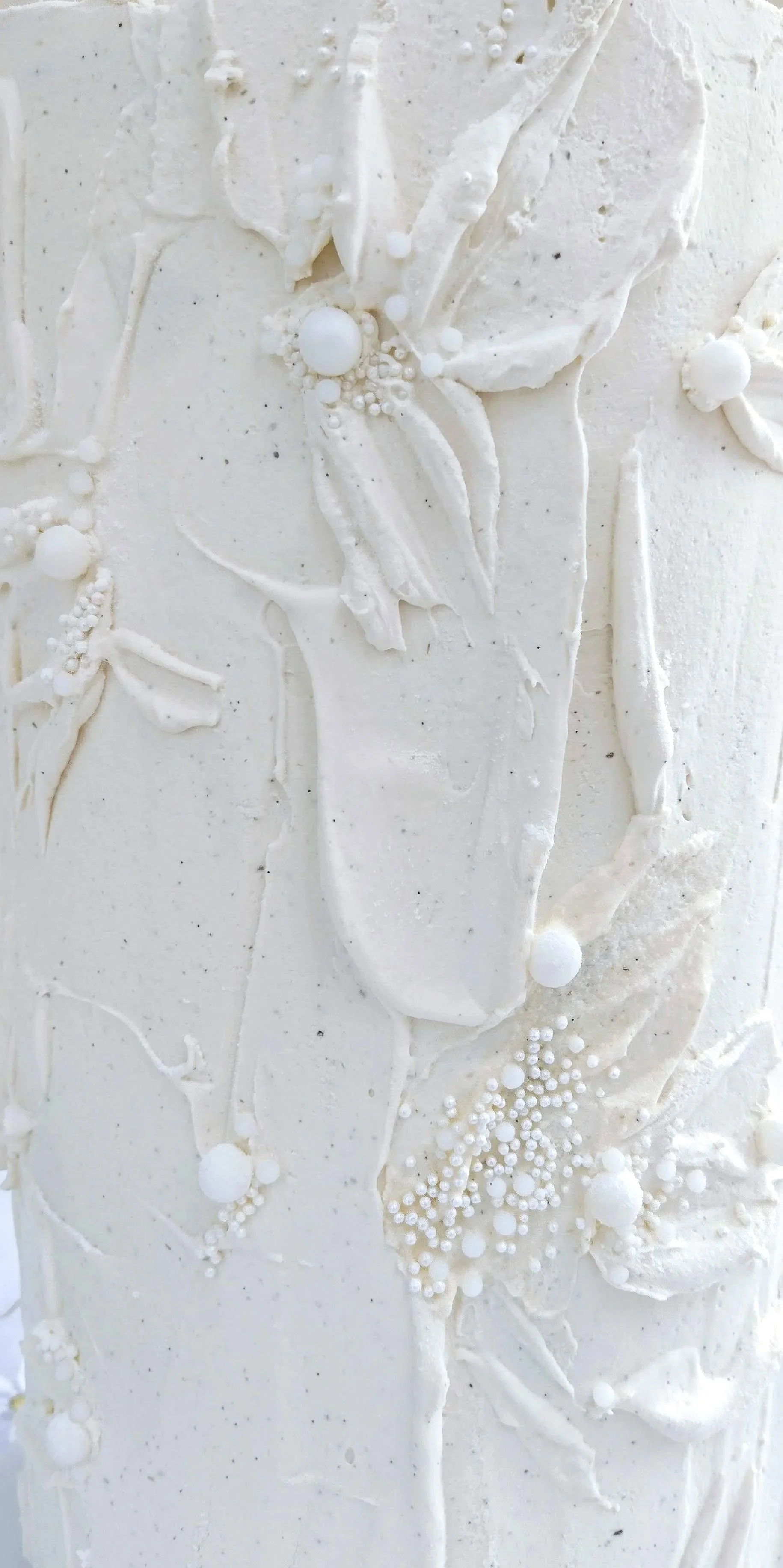 White chocolate ganache, expertly applied to resemble the gentle folds and movement of draped fabric, creating a soft and sculptural finish. Delicate knife petal work adds an element of artistry and texture, while subtle pinhead pearls provide a refi
