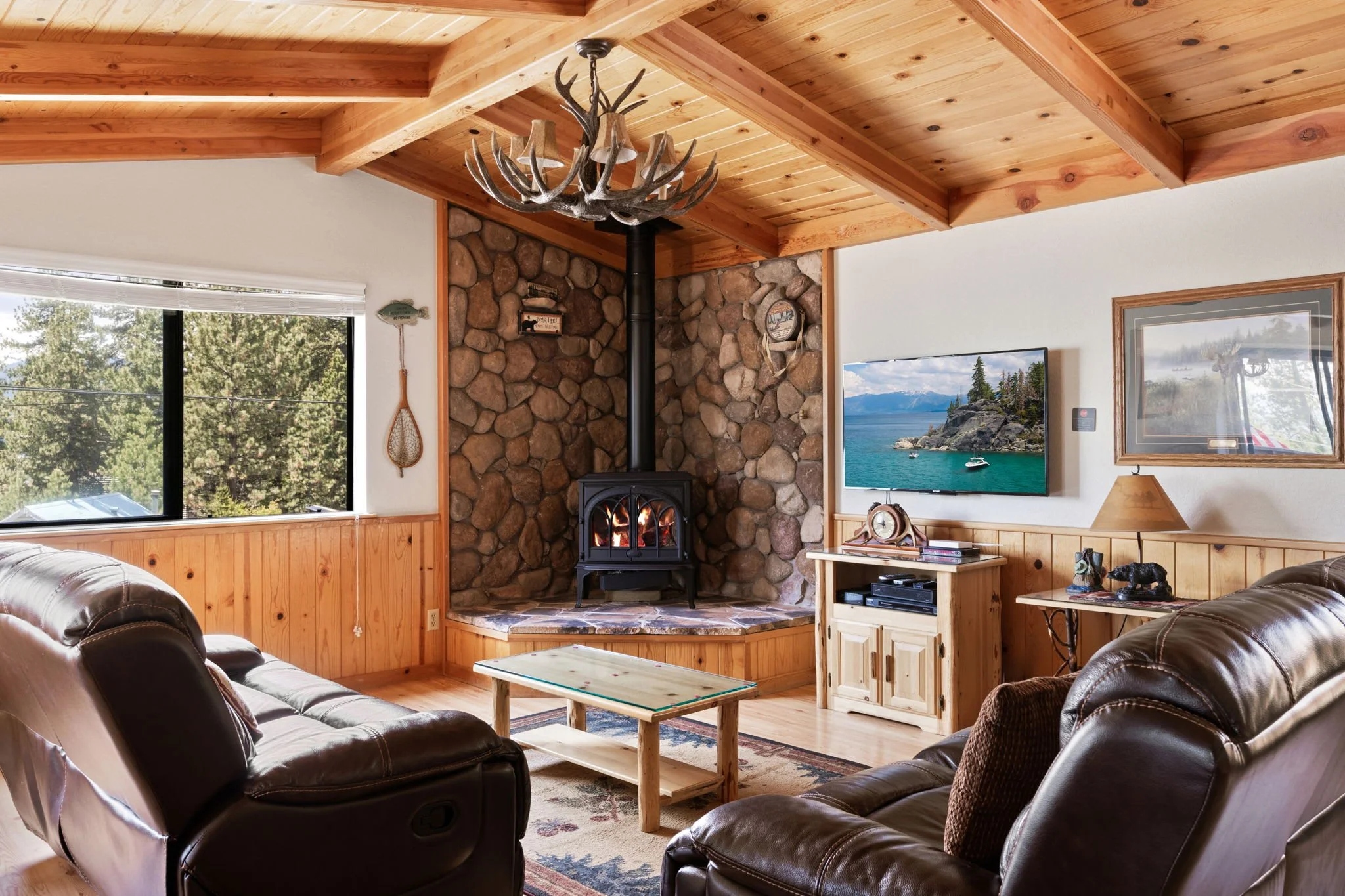 Cozy cabin living room with leather sofas, light wood ceilings and furnishings and a chiminea as the focal point. Picture of Lake Tahoe on the wall