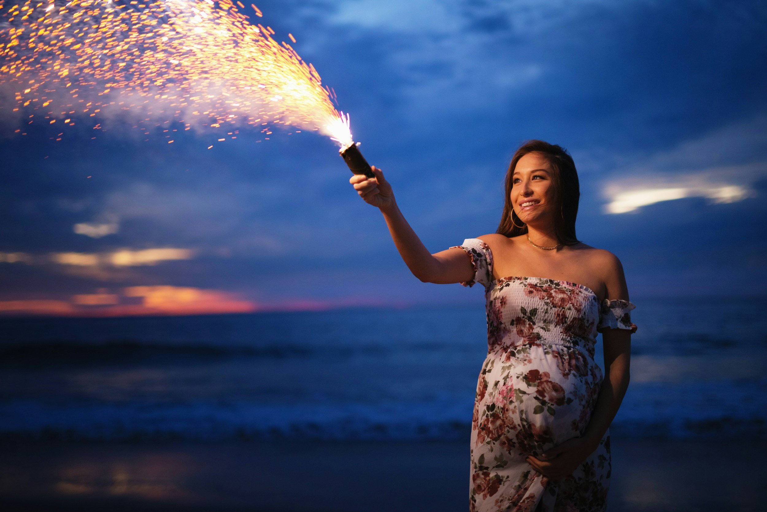 Pregnant woman holding a sparkler on the beach at dusk, symbolizing hope and support before postpartum.