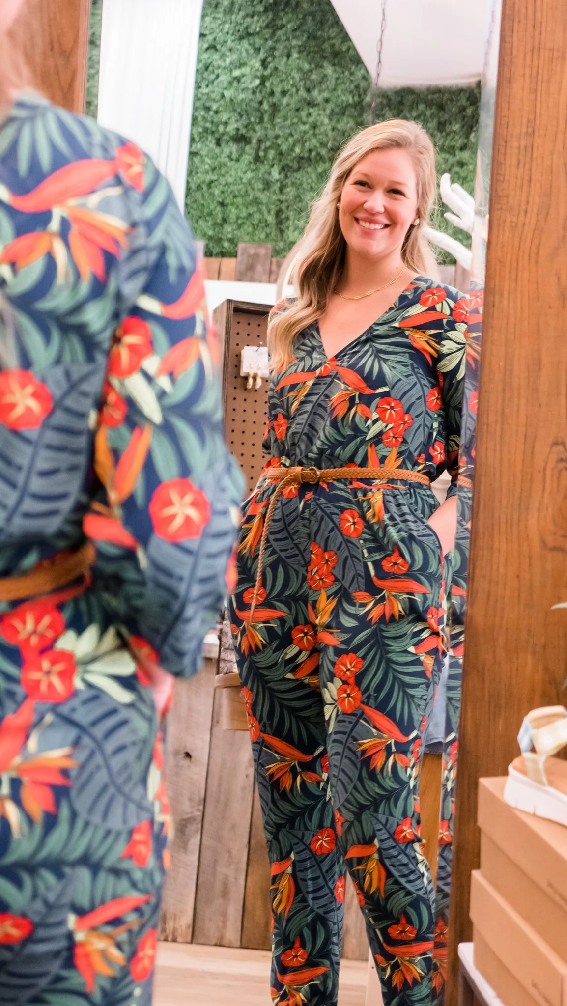 Blonde woman smiling in a mirror while trying on stylish boutique clothing – elegant fashion photography capturing a joyful shopping experience.