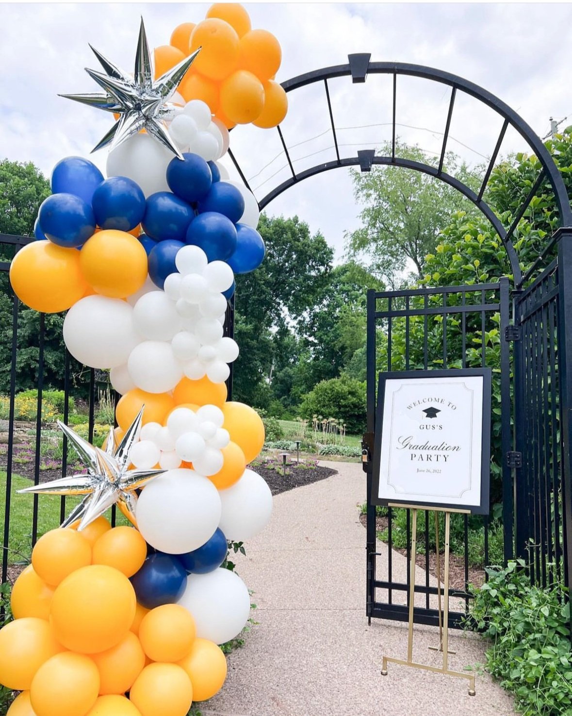 A white, blue, and gold graduation party balloon garland with silver starburst balloons