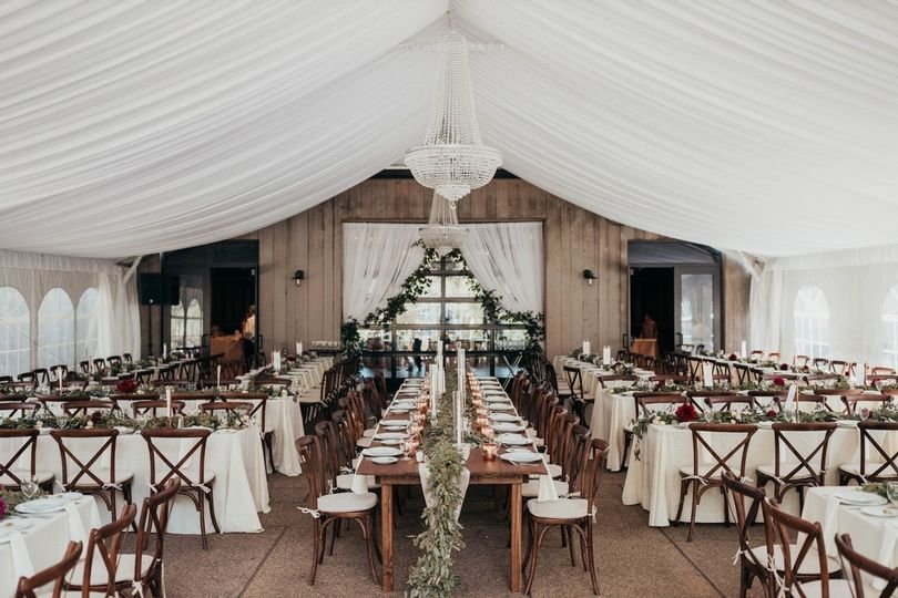 Pittsburgh Botanical Garden's text space decorated for a wedding with wooden tables and chairs, white table decor, and greenery and candles spread across tables.