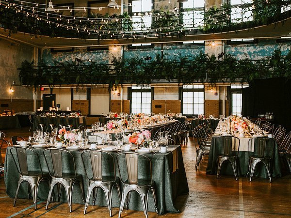 "The Gym" event space at the Ace Hotel decorated for a formal event with dark green tablecloths, florals, and fairy lights.