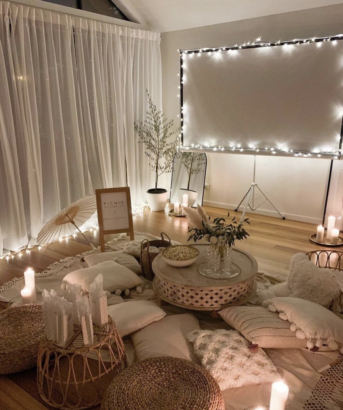 An at-home movie set up with a projector, fairy lights, pillows, blankets, and candles