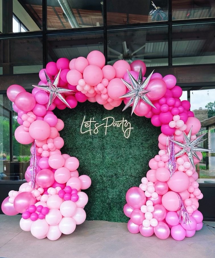 pink organic balloon arch on photo wall stating "let's party"