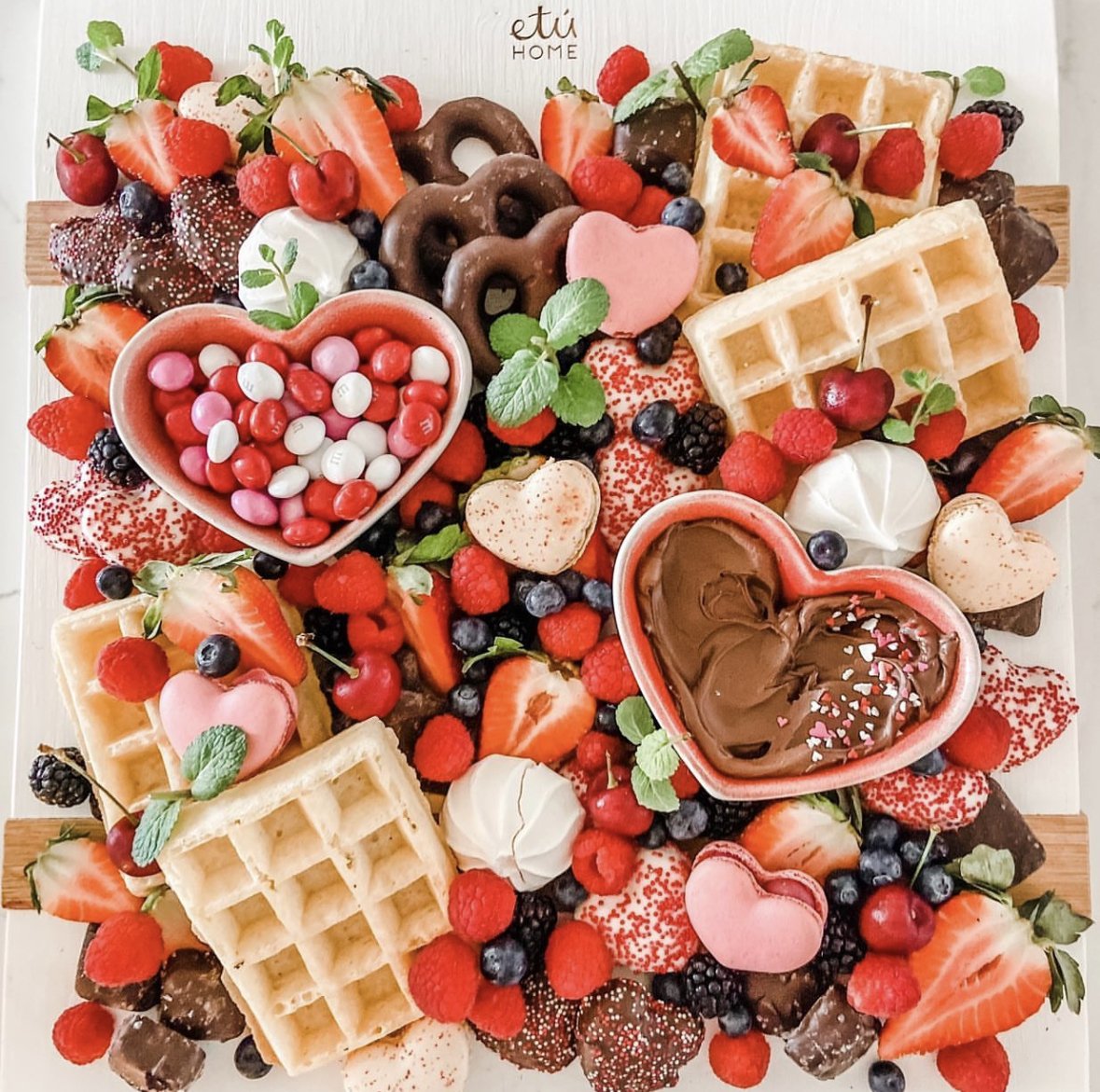 A Valentine's themed grazing board with waffles, berries, candy, and chocolate.