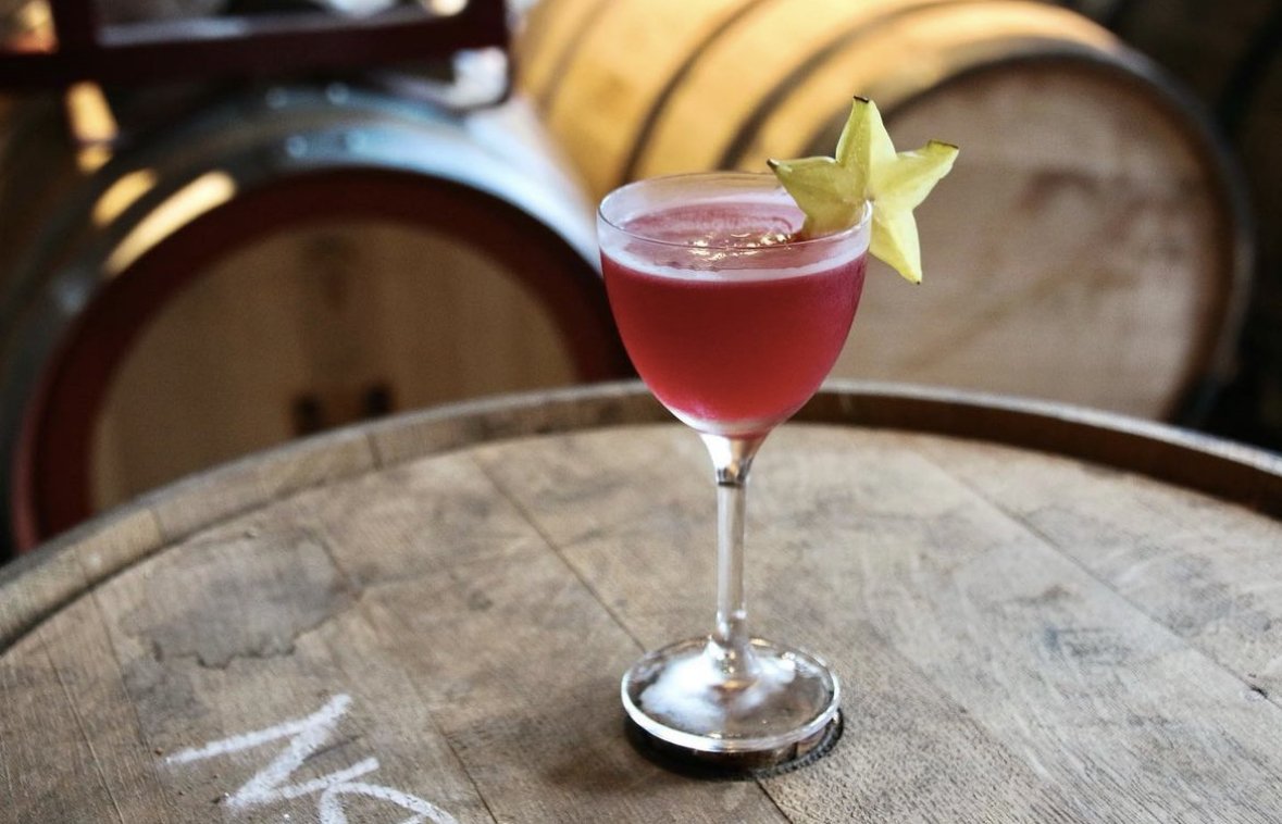 A red cocktail with a starfruit in it sitting on a barrel at Kingfly Spirits in Pittsburgh.