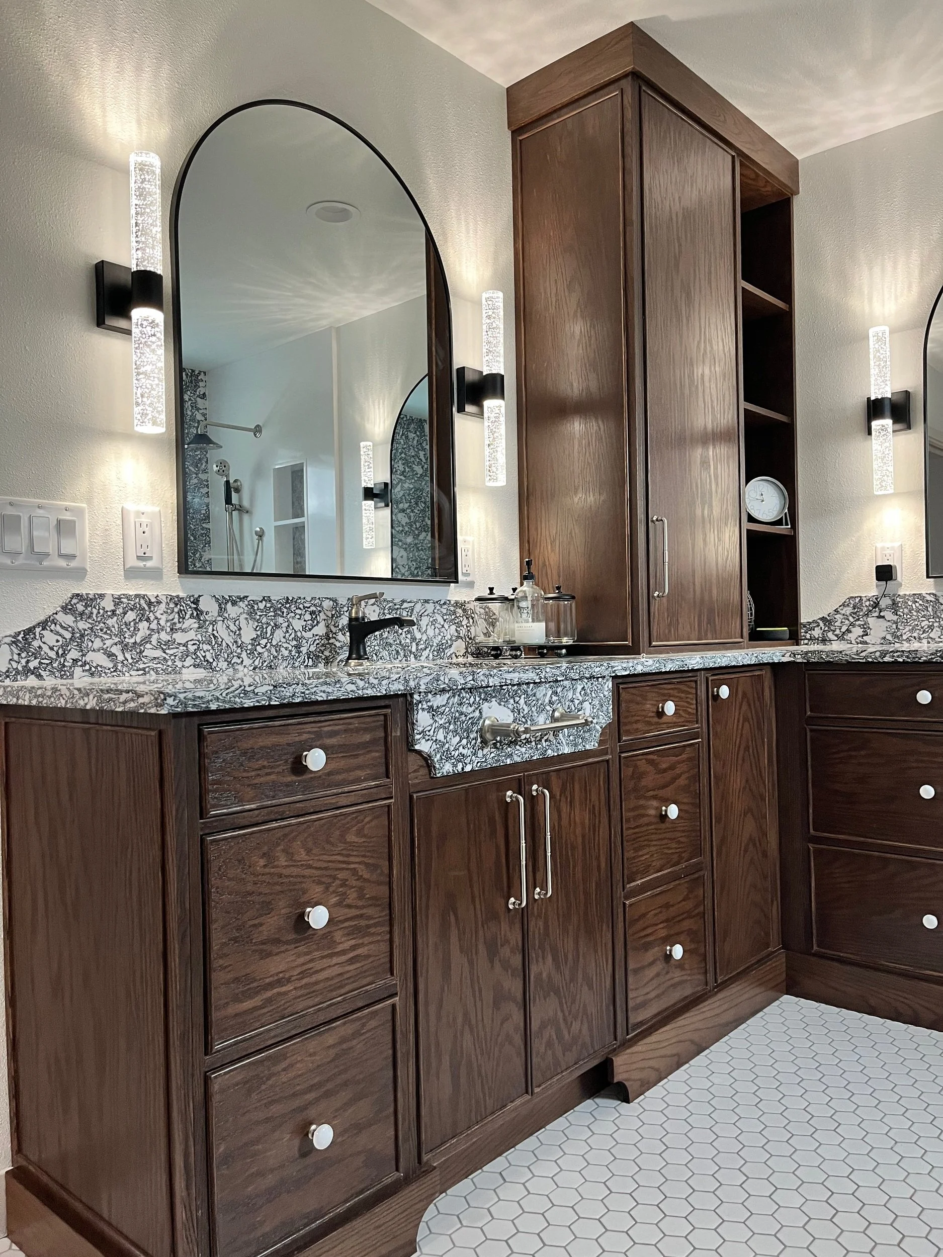 Wooden bathroom vanity with a granite countertop, a mirror, and wall-mounted lights.