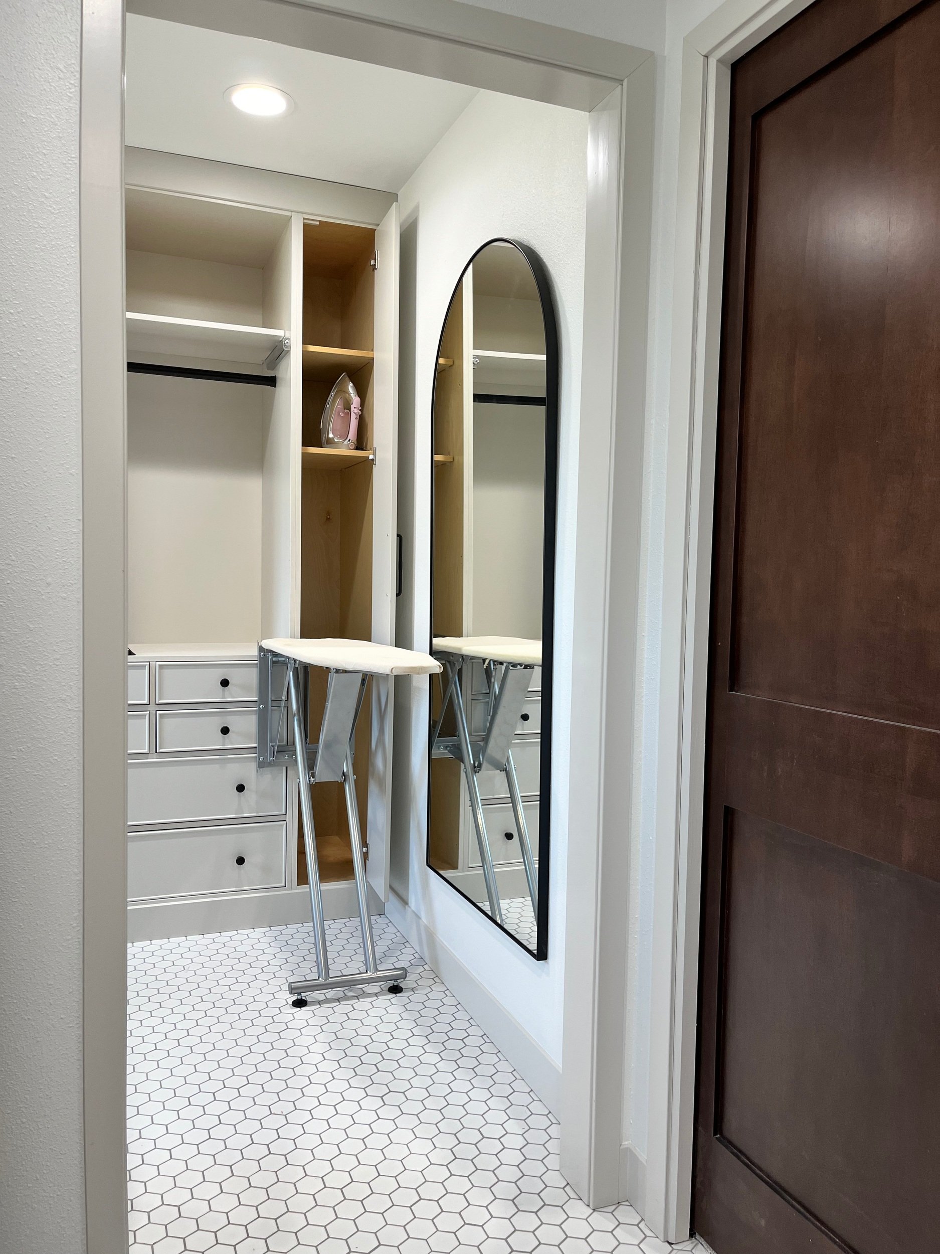 Walk-in closet with white shelves, two chairs, a large mirror, and hexagonal white floor tiles.