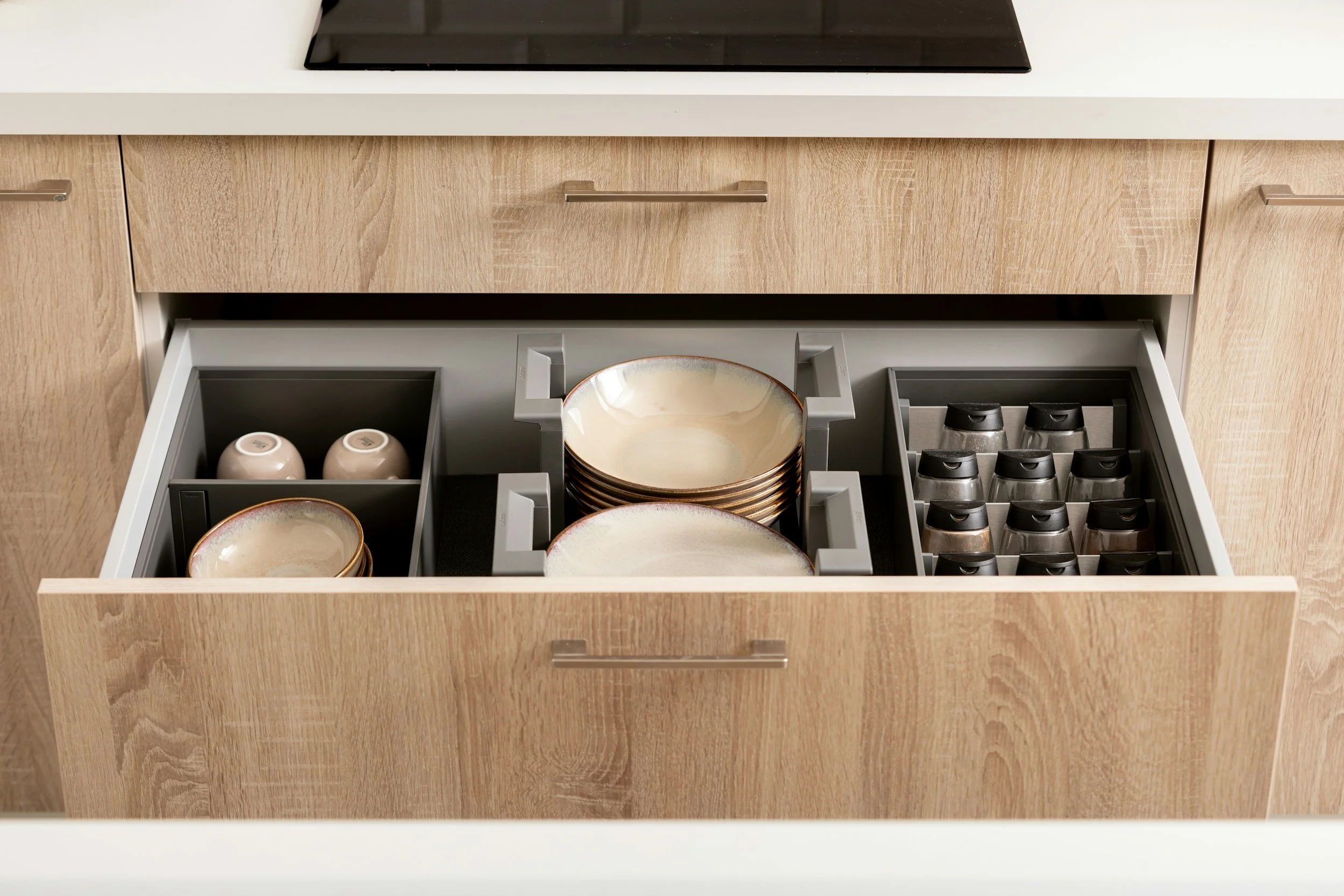 Open kitchen drawer containing stacked ceramic bowls, small cups, and coffee pods.