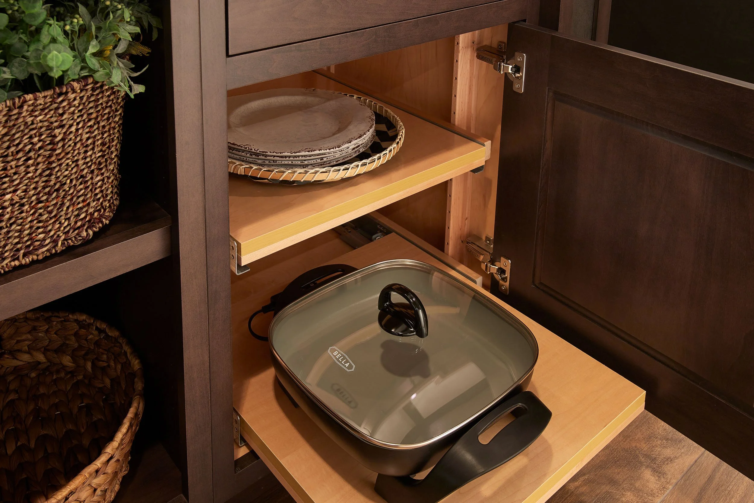 Open kitchen cabinet with plates on a tray and an electric skillet inside.