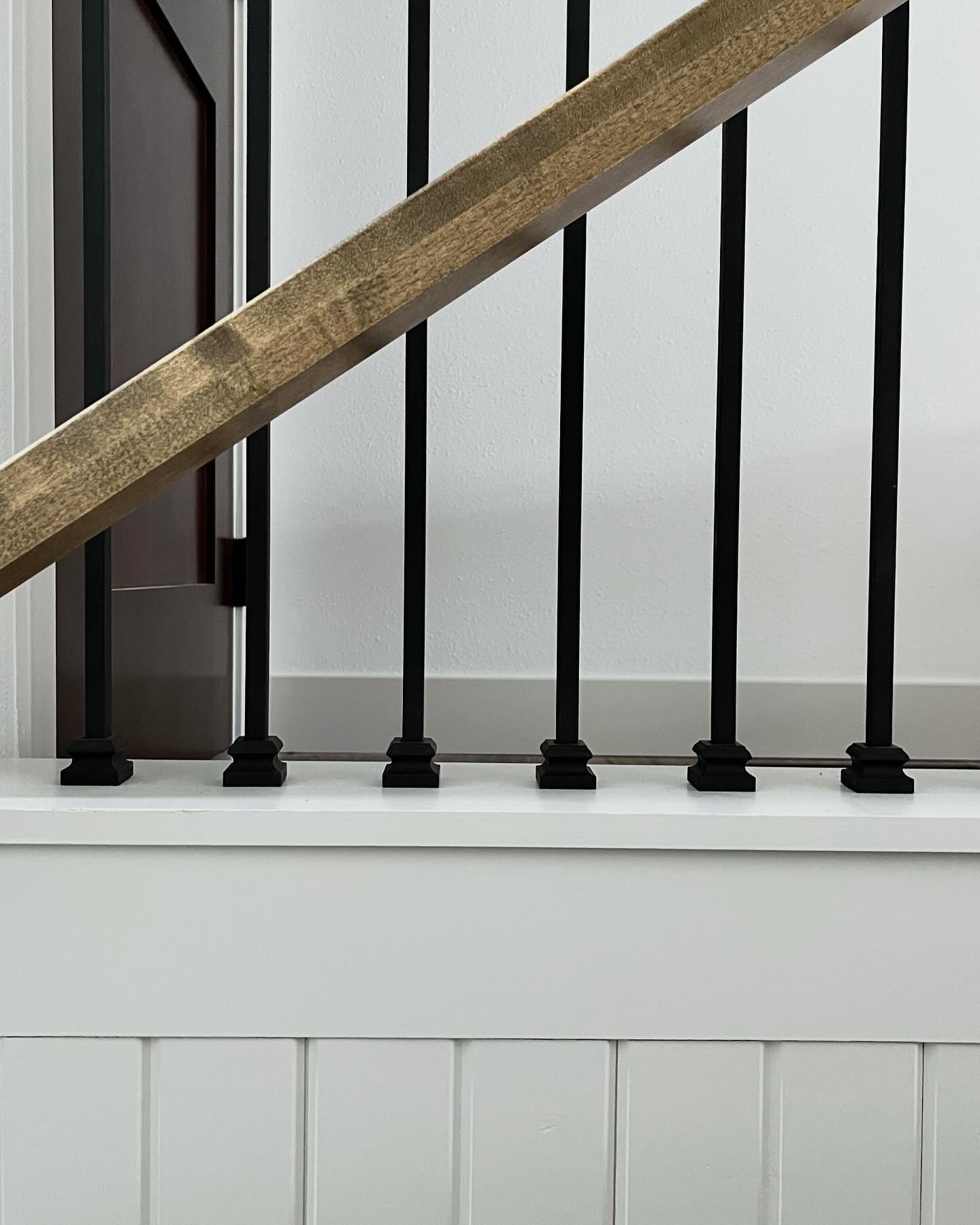 Black metal staircase railing with a wooden handrail. Shiplap tongue and grove wall.