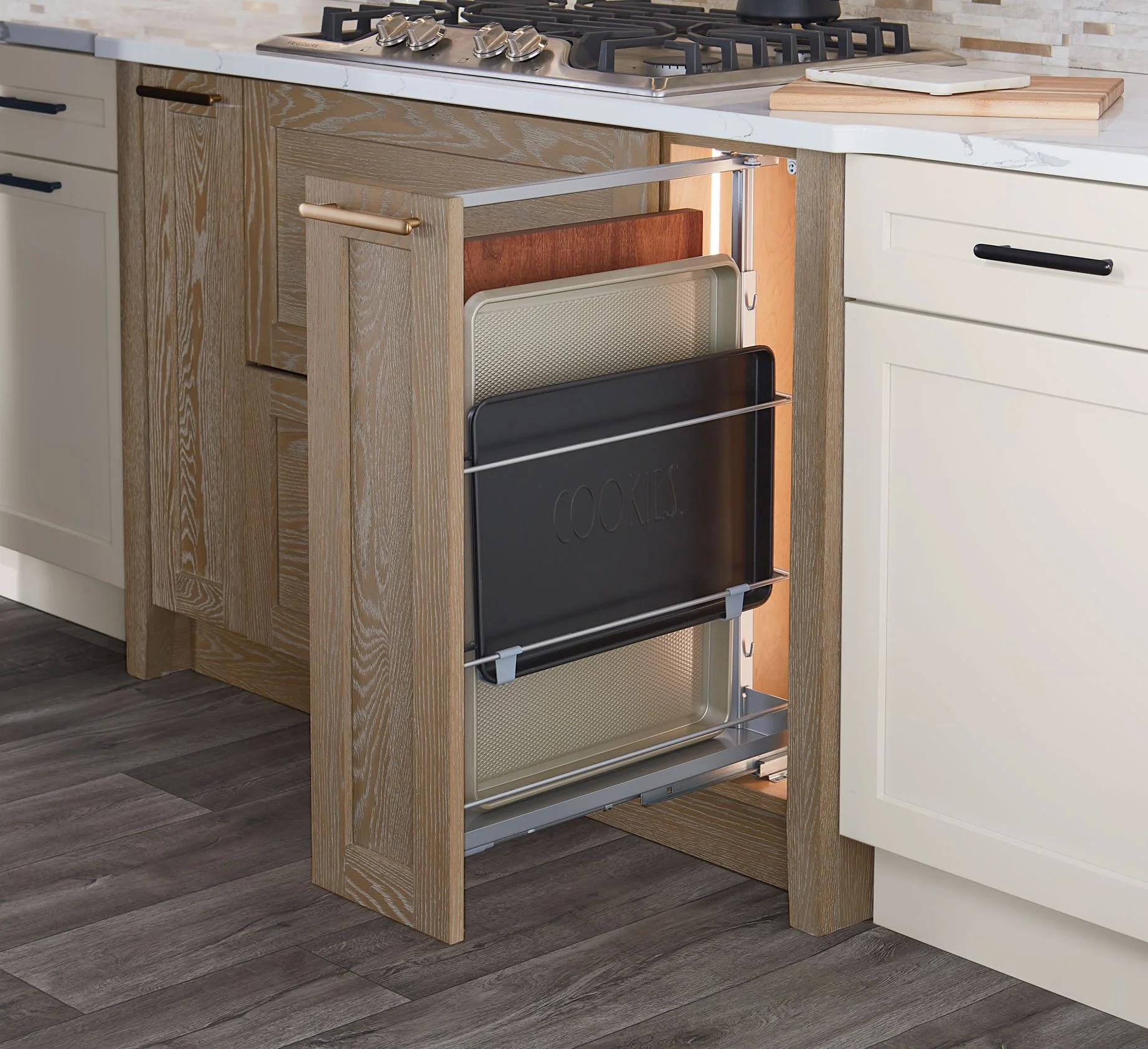 Open kitchen cabinet with metal trays labeled 'Cookies' and 'Snacks' inside, next to a stove and cutting boards.