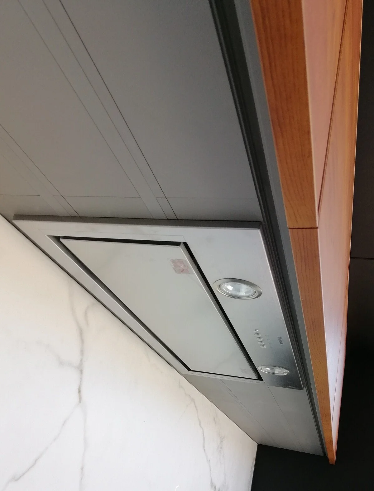 Close-up of a modern stainless steel dishwasher built into a kitchen cabinet with a wooden countertop above it, and a marble countertop in the foreground.