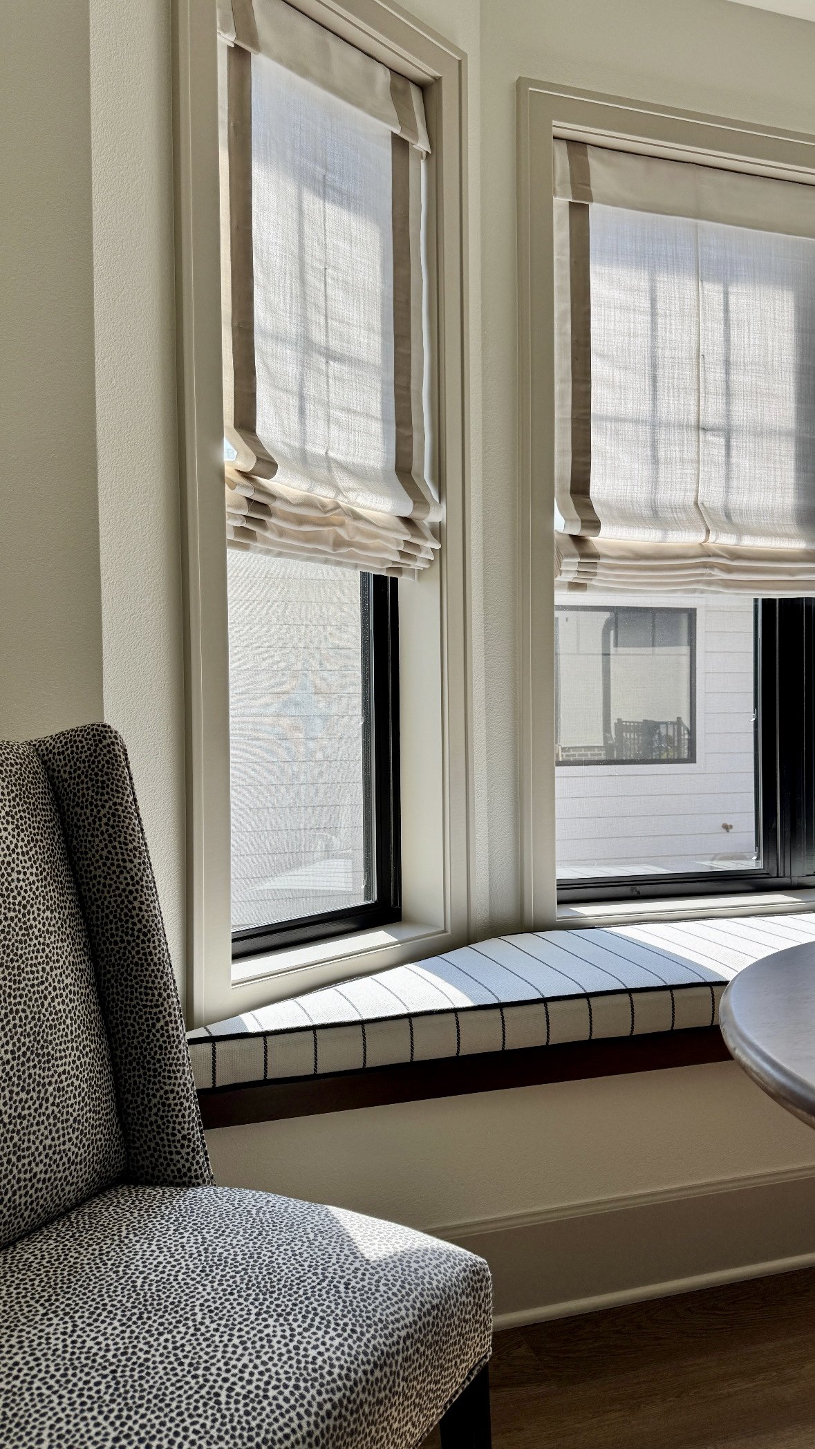 A sitting area with a window seat, a speckled fabric armchair, and two windows with white shades.