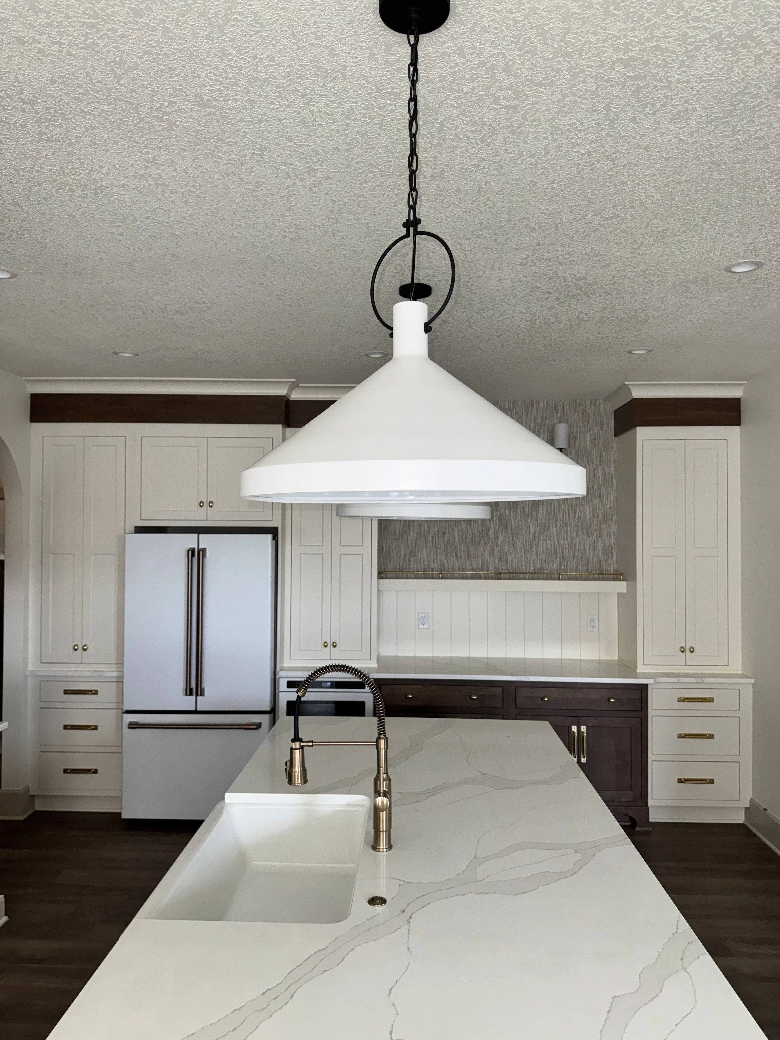 Modern kitchen with white cabinets, a white marble island with gold hardware, a white pendant light, and a stainless steel refrigerator.