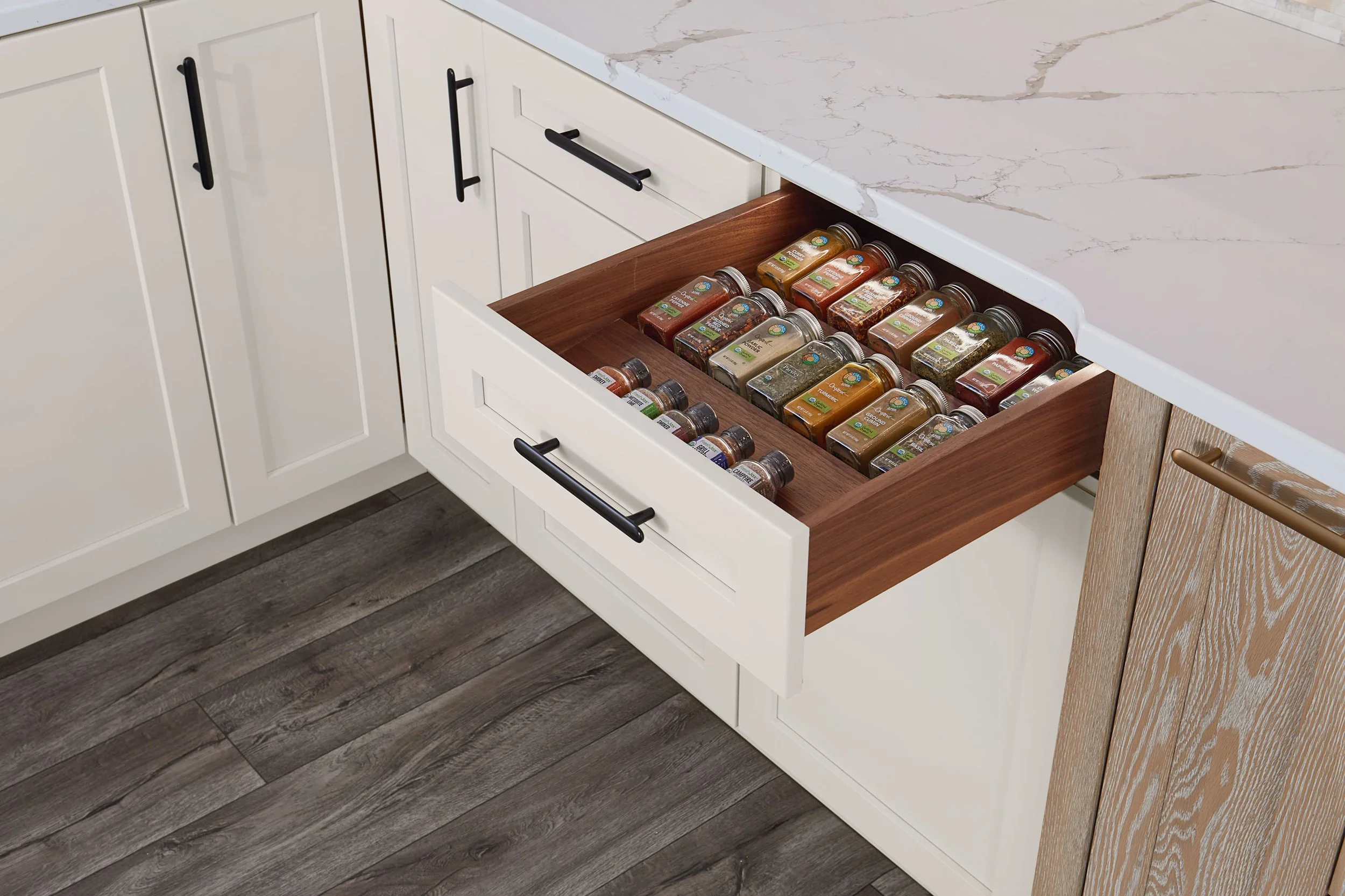 Open kitchen drawer filled with spice jars and bottles on a pull-out wooden tray.