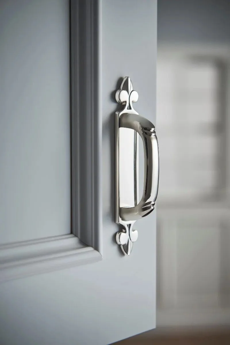 Close-up of a silver drawer handle with decorative accents on a gray cabinet door.