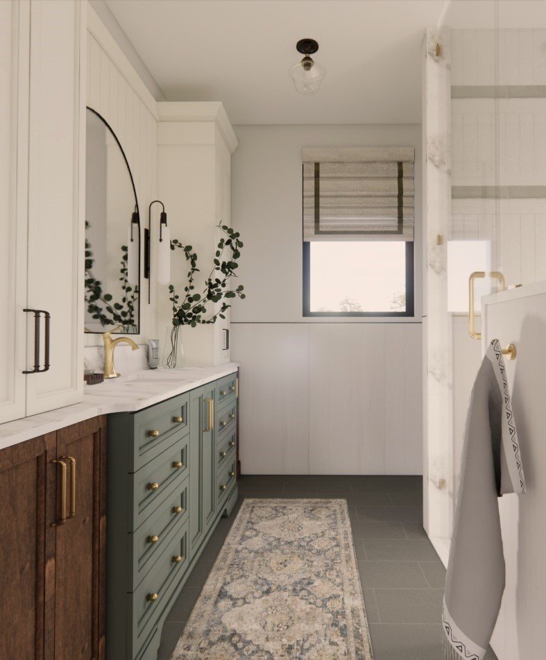 A modern bathroom with white upper cabinets, dark green lower cabinets with gold handles, a marble countertop, a large mirror, a small window with a Roman shade, a patterned rug on dark tiled floors, and a towel hanging on a rack.