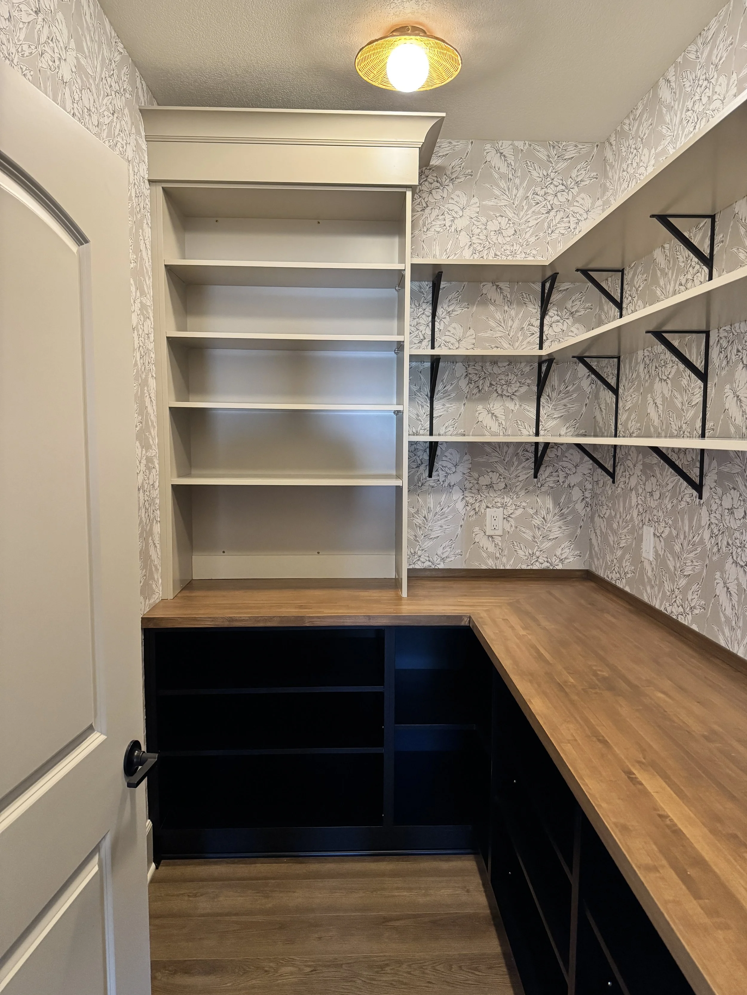 Empty pantry or storage room with built-in shelves, desk space, and wallpaper with a leaf pattern.