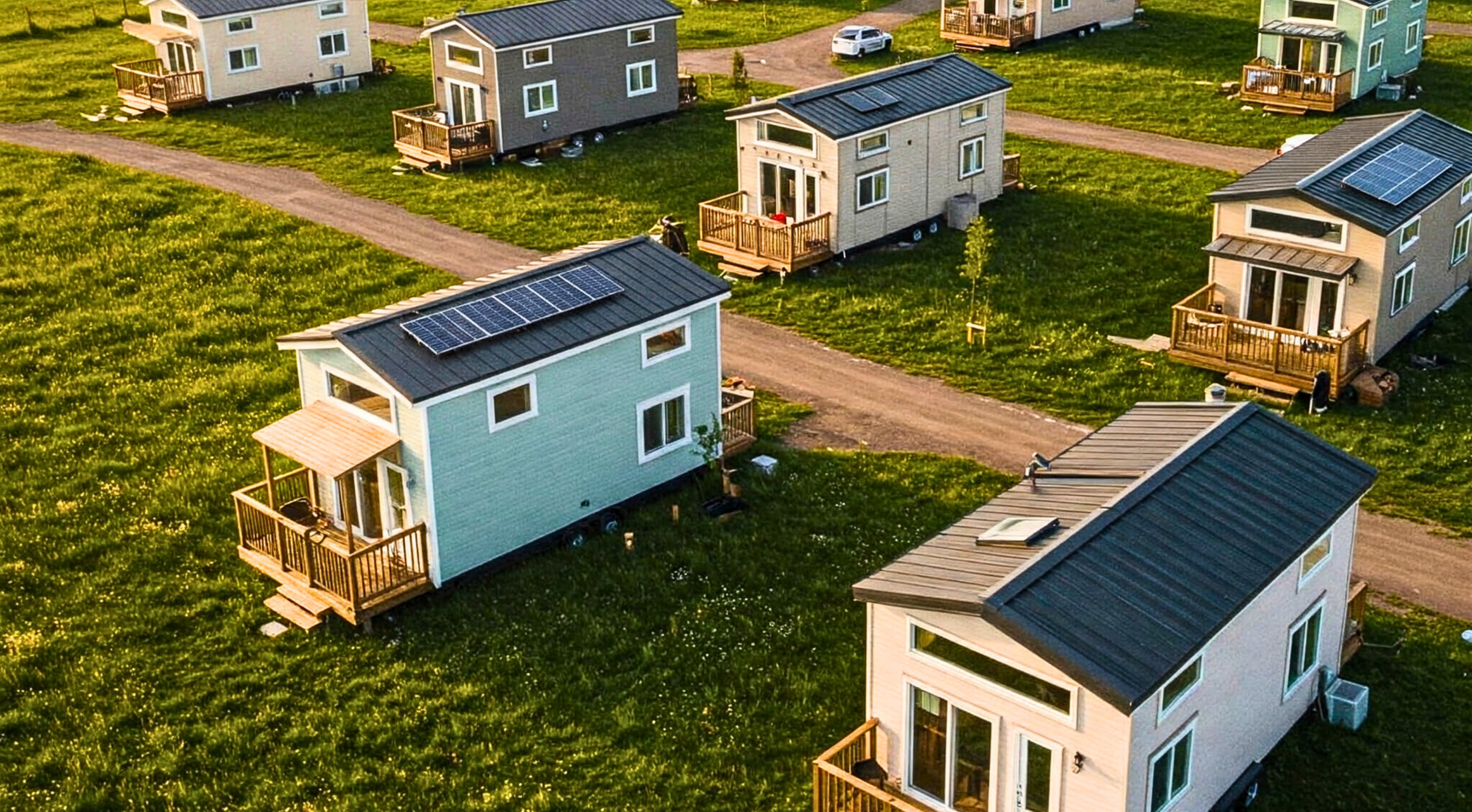 Interior of a cozy camper van with a wooden ceiling and walls, kitchenette, and bed. A guitar leans against the bed, and a window offers a view of green trees.