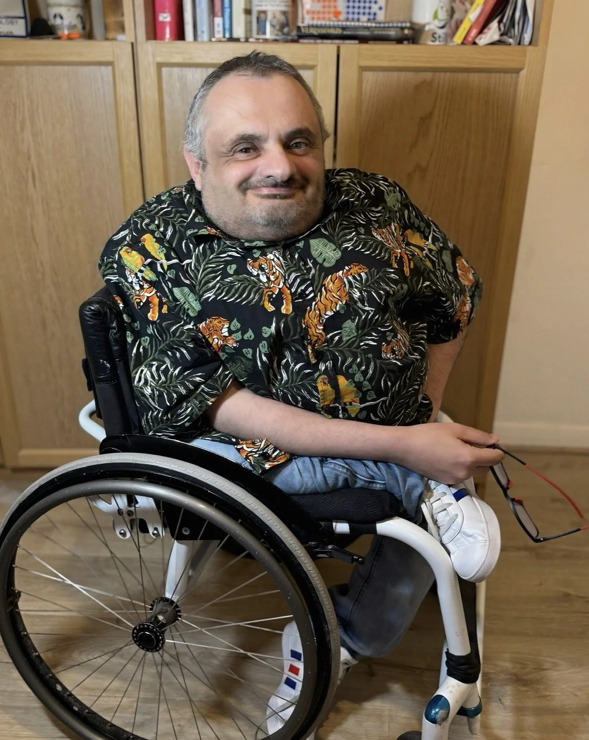 Stuart Thompson founder and creator of the STILL Method. He is in his office bookshelf is behind him and he wears colourful shirt.  Stuart is a little person in a wheelchair