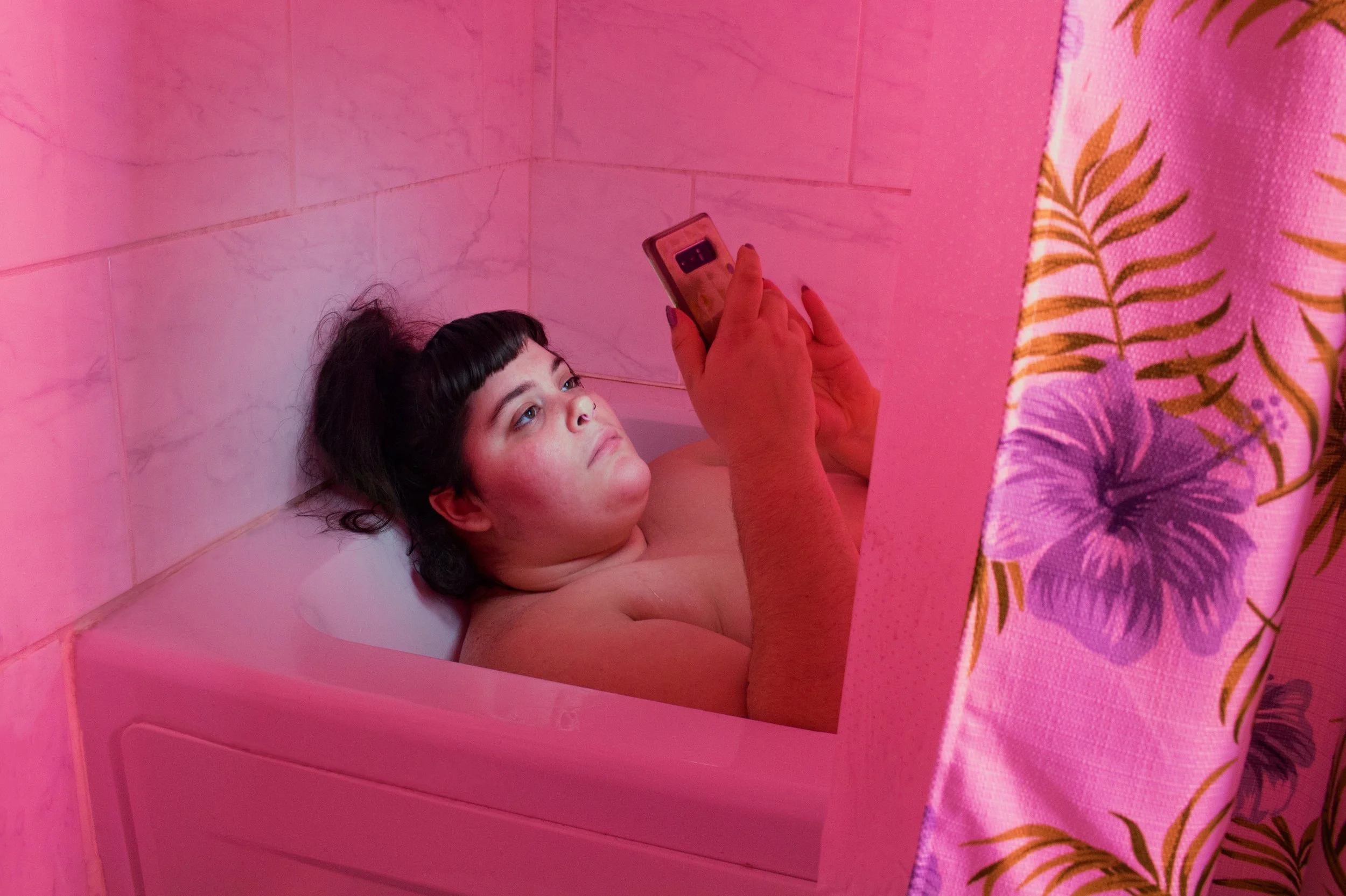 the artist laying in a bathtub, looking at her phone
