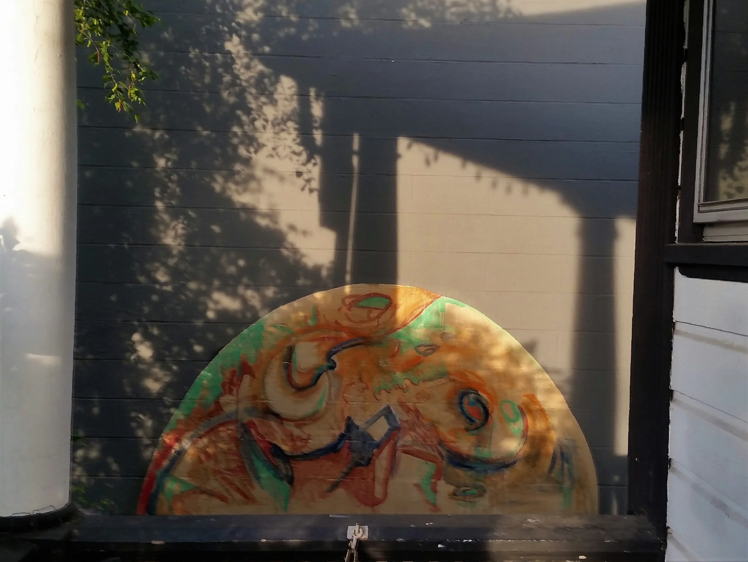 A large, colorful abstract painting on a half circle shaped piece of wood, sitting on an outdoor porch