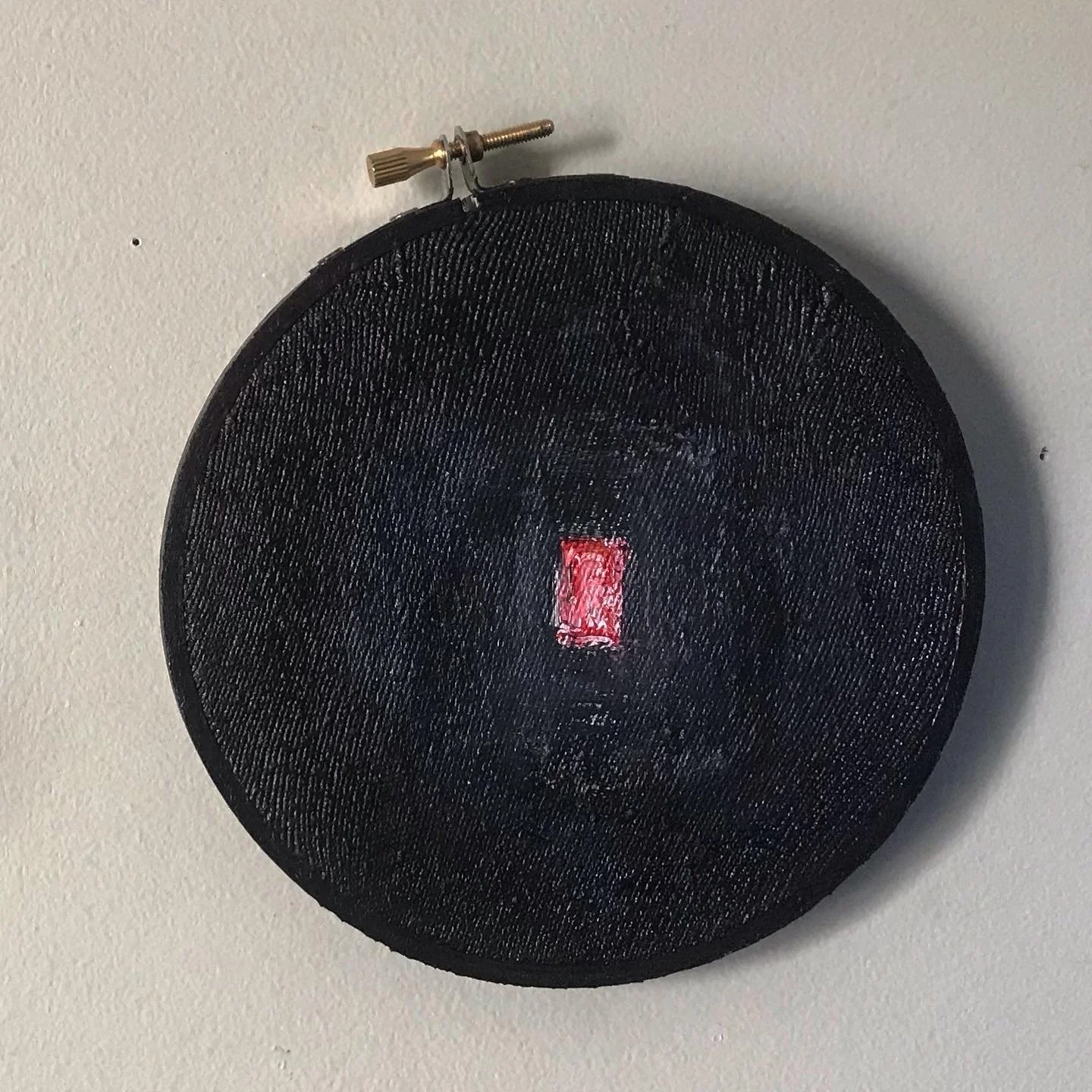 stretched on an embroidery loop, a deep black painting with a small red square in the center