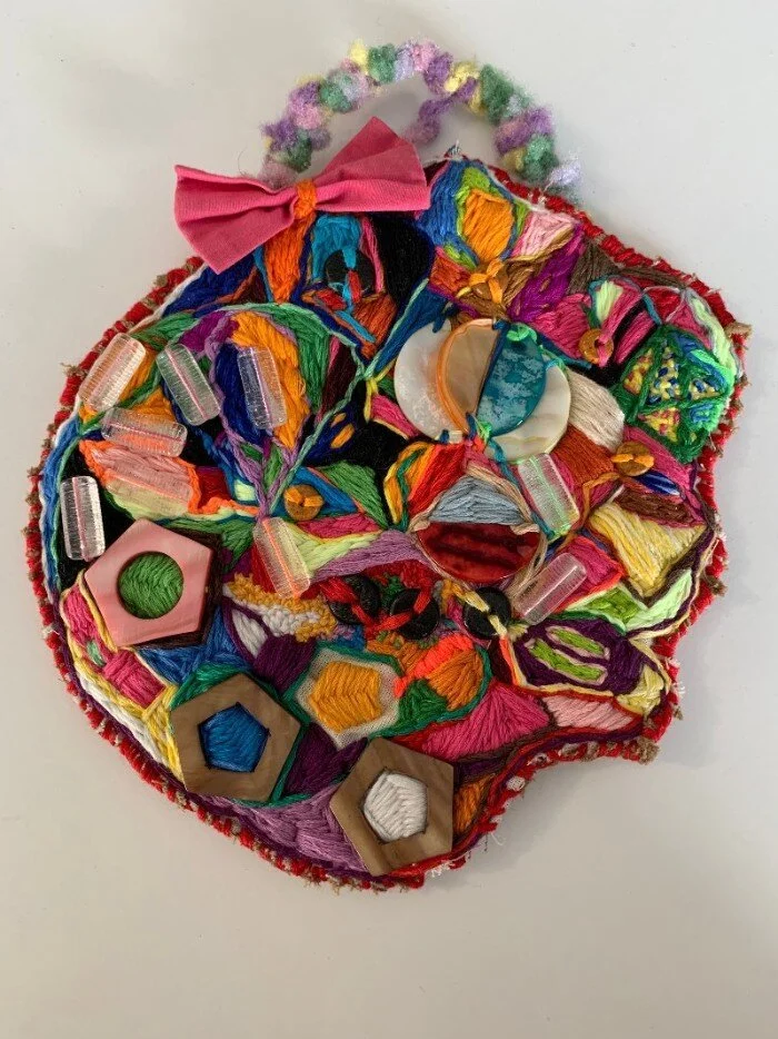 An abstract, colorful embroidery artwork with large beads and wooden object sewn throughout