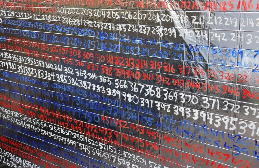 Seen at a slight angle is a photo of long strings of number written horizontally in red, white, and blue
