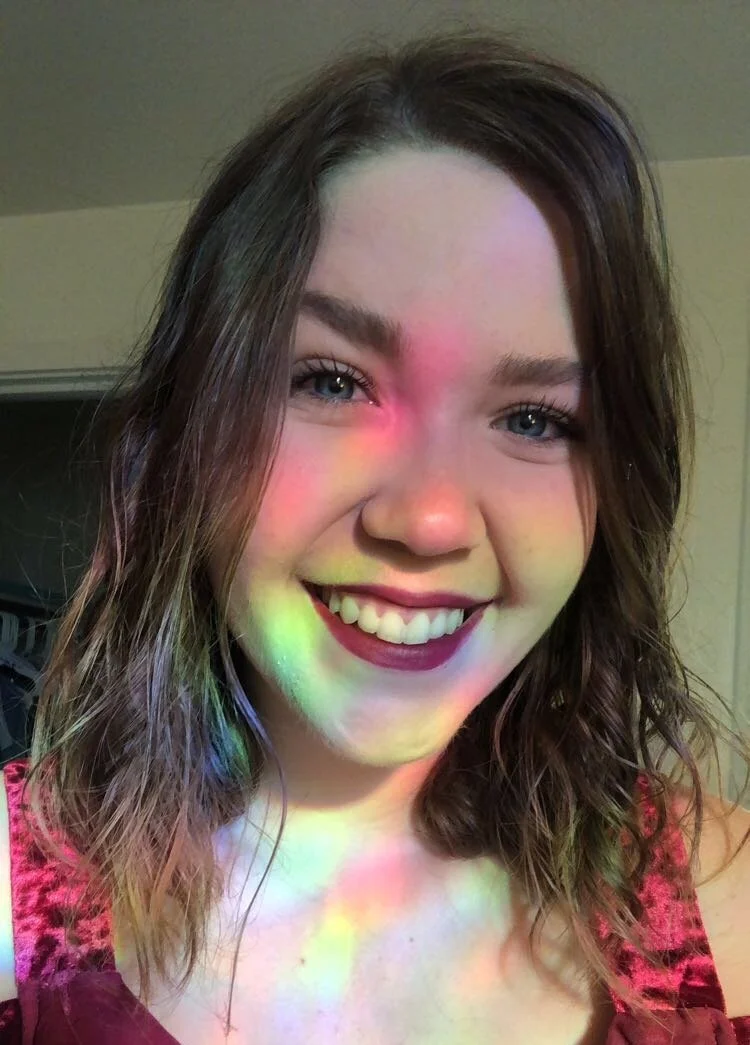 Headshot of a white femme person with wavy brown hair smiling.